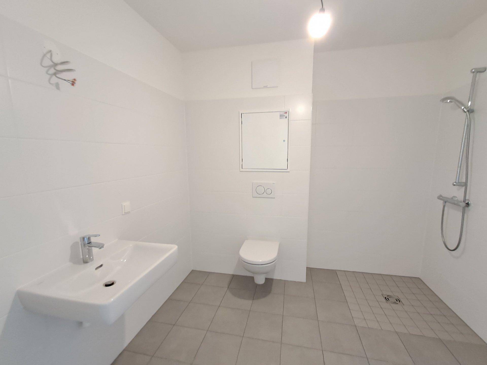 Helles Badezimmer mit Dusche, Wand-WC und großformatigen Fliesen.