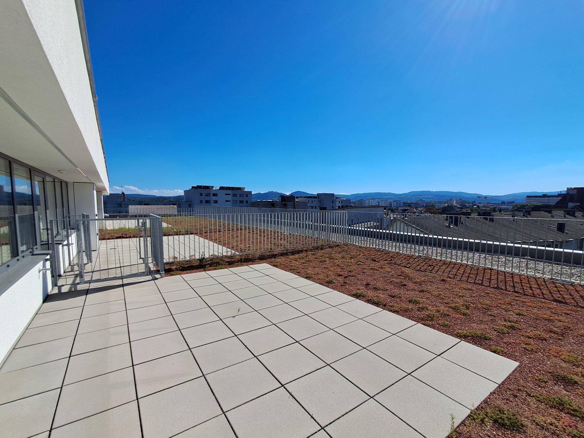 Weitläufige Dachterrasse mit Fliesen und Grünflächen, bietet einen weiten Blick.