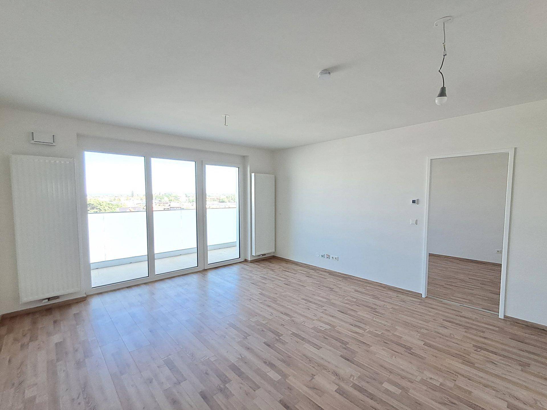 Lichtdurchfluteter Wohnbereich mit Holzboden und großem Fenster mit Balkonzugang.