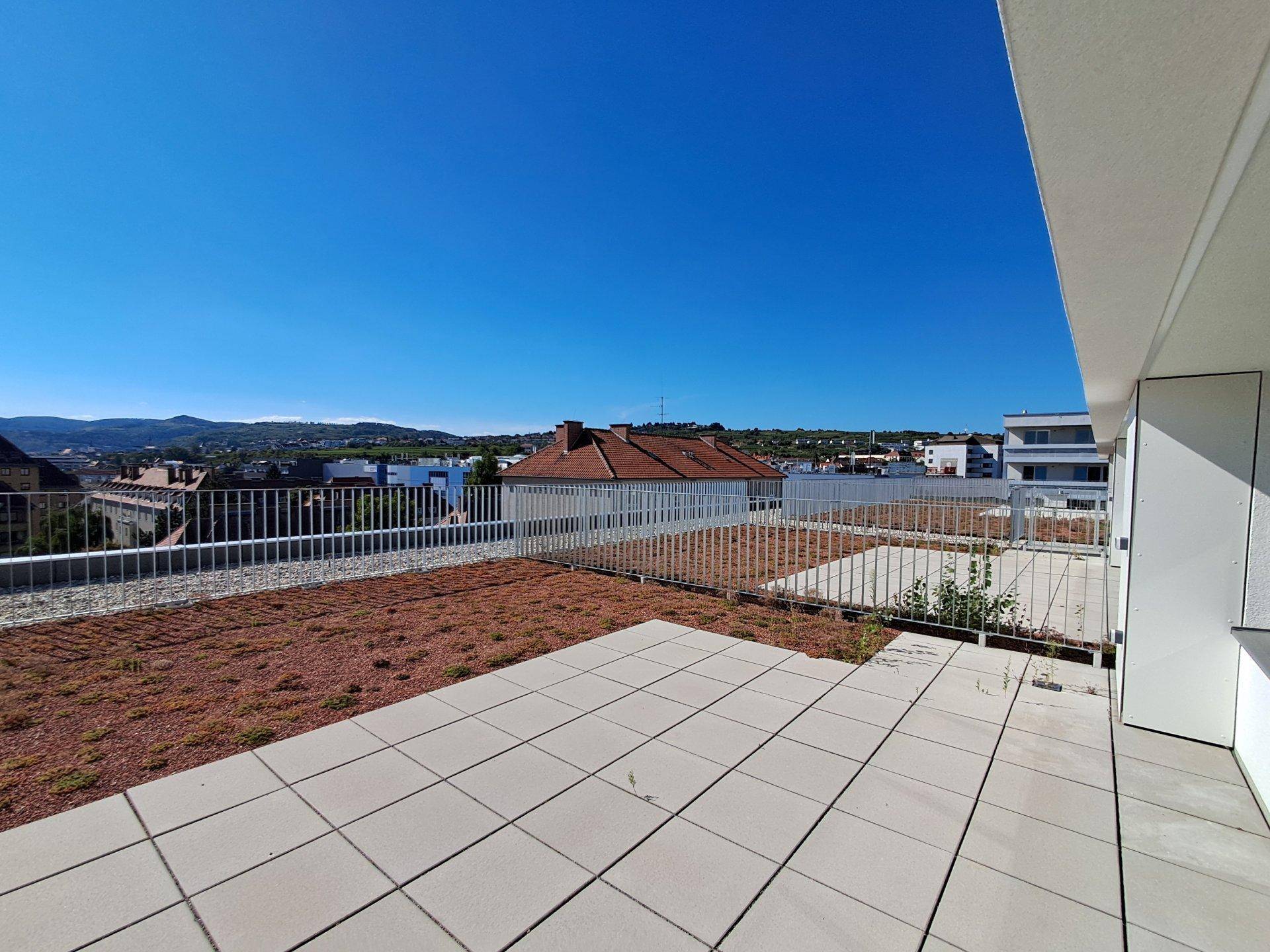 Geräumige Dachterrasse mit Fliesen und Begrünung, umgeben von einer modernen Architektur.