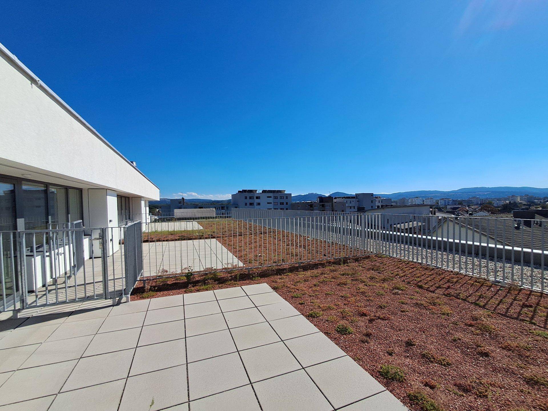 Helle Dachterrasse mit Fliesen und Grünflächen, bietet einen Panoramablick über die Stadt.