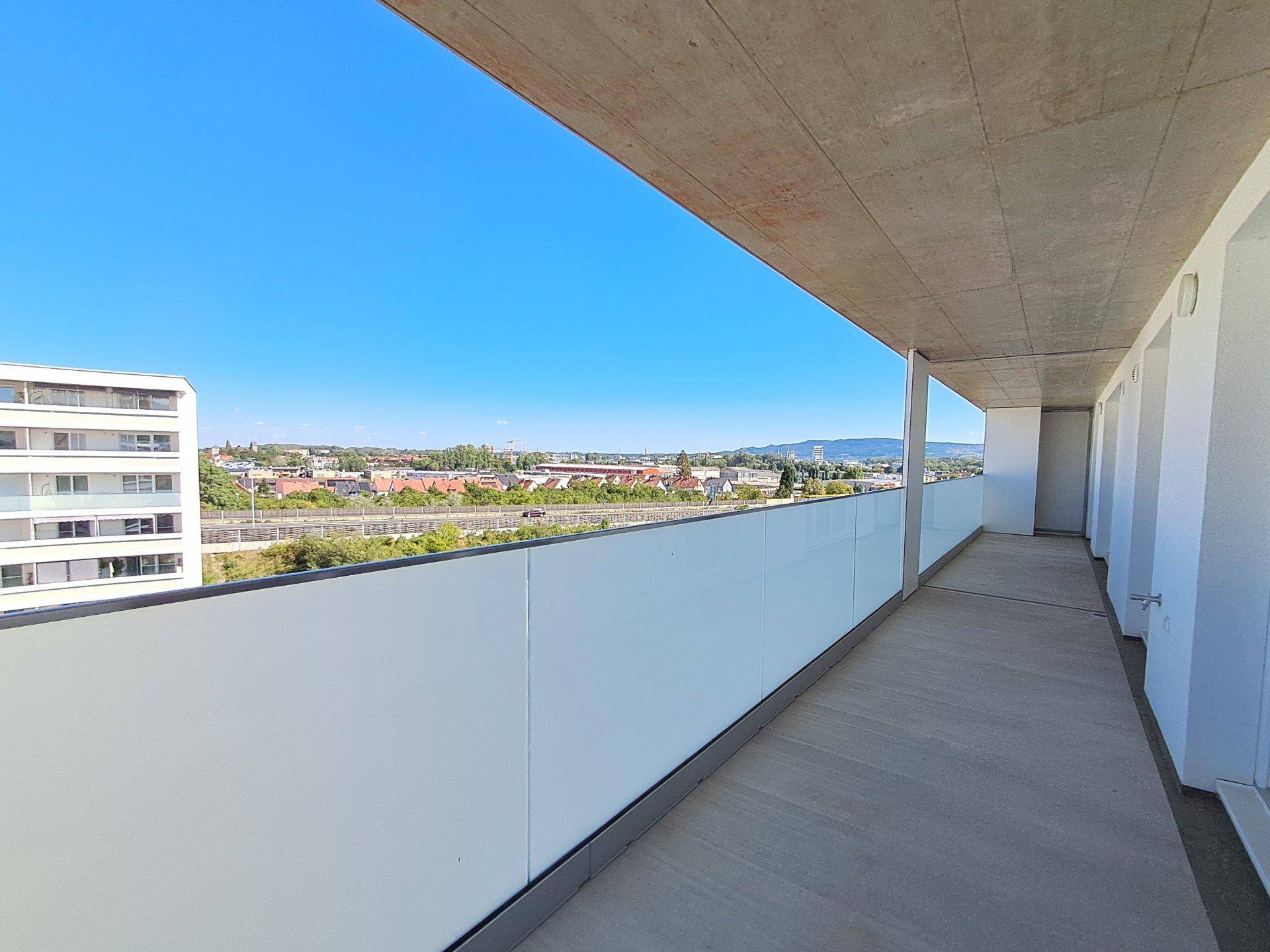 Langer Balkon mit Glasbrüstung und weitem Blick über die Stadt und Landschaft.