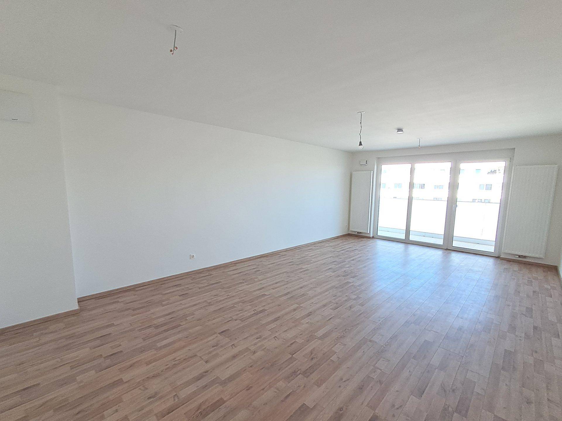 Geräumiger, heller Raum mit Laminatboden und großem Fenster zum Balkon.