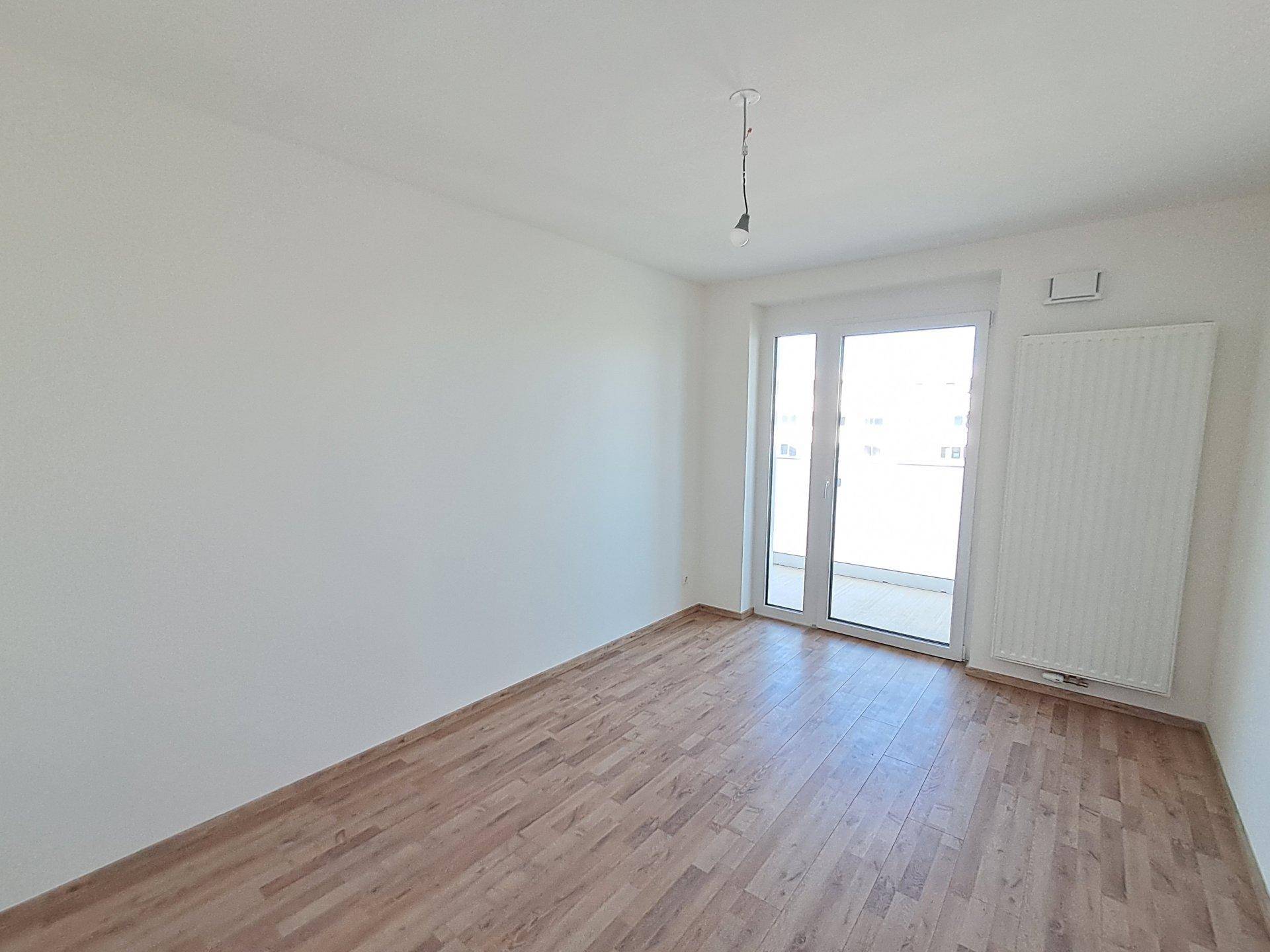 Leeres Schlafzimmer mit Laminatboden, weißen Wänden und direktem Zugang zum Balkon.