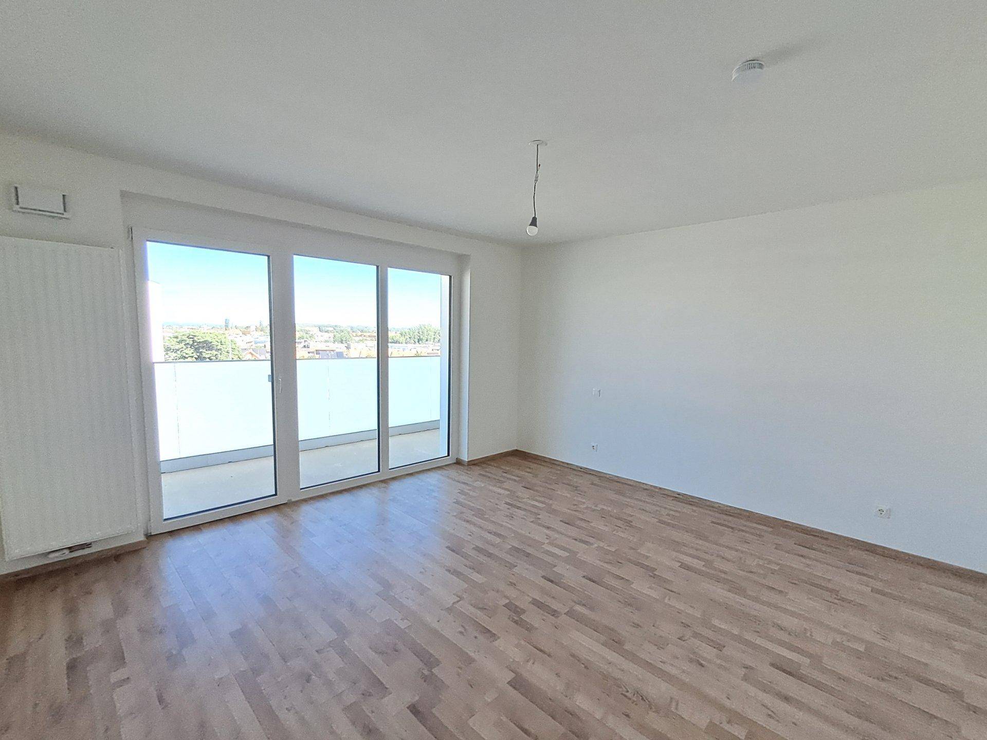 Geräumiges, helles Zimmer mit Laminatboden und großem Fenster zum Balkon.
