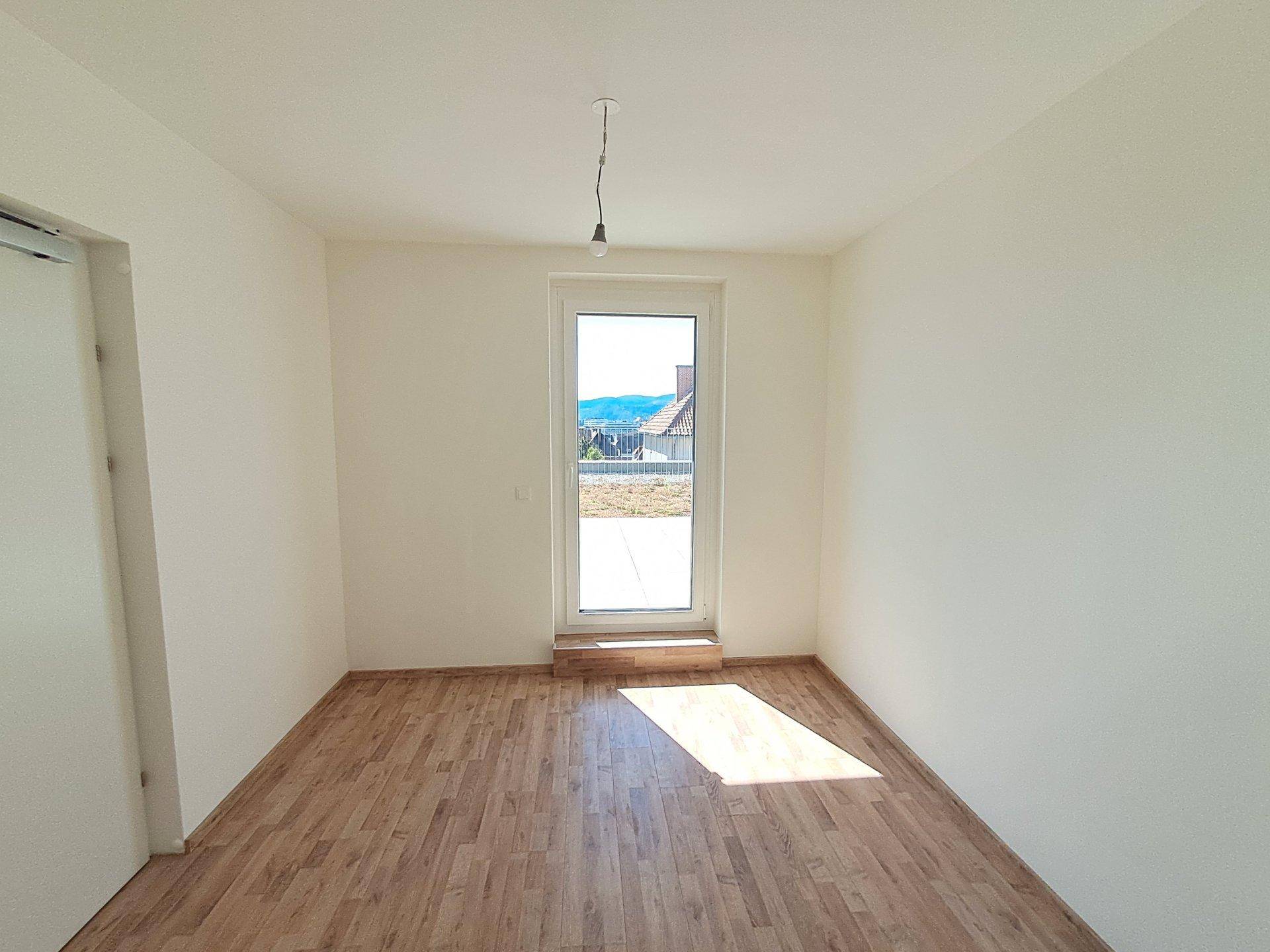Heller Raum mit Laminatboden und Tür zu einem Außenbereich, bietet viel Tageslicht.