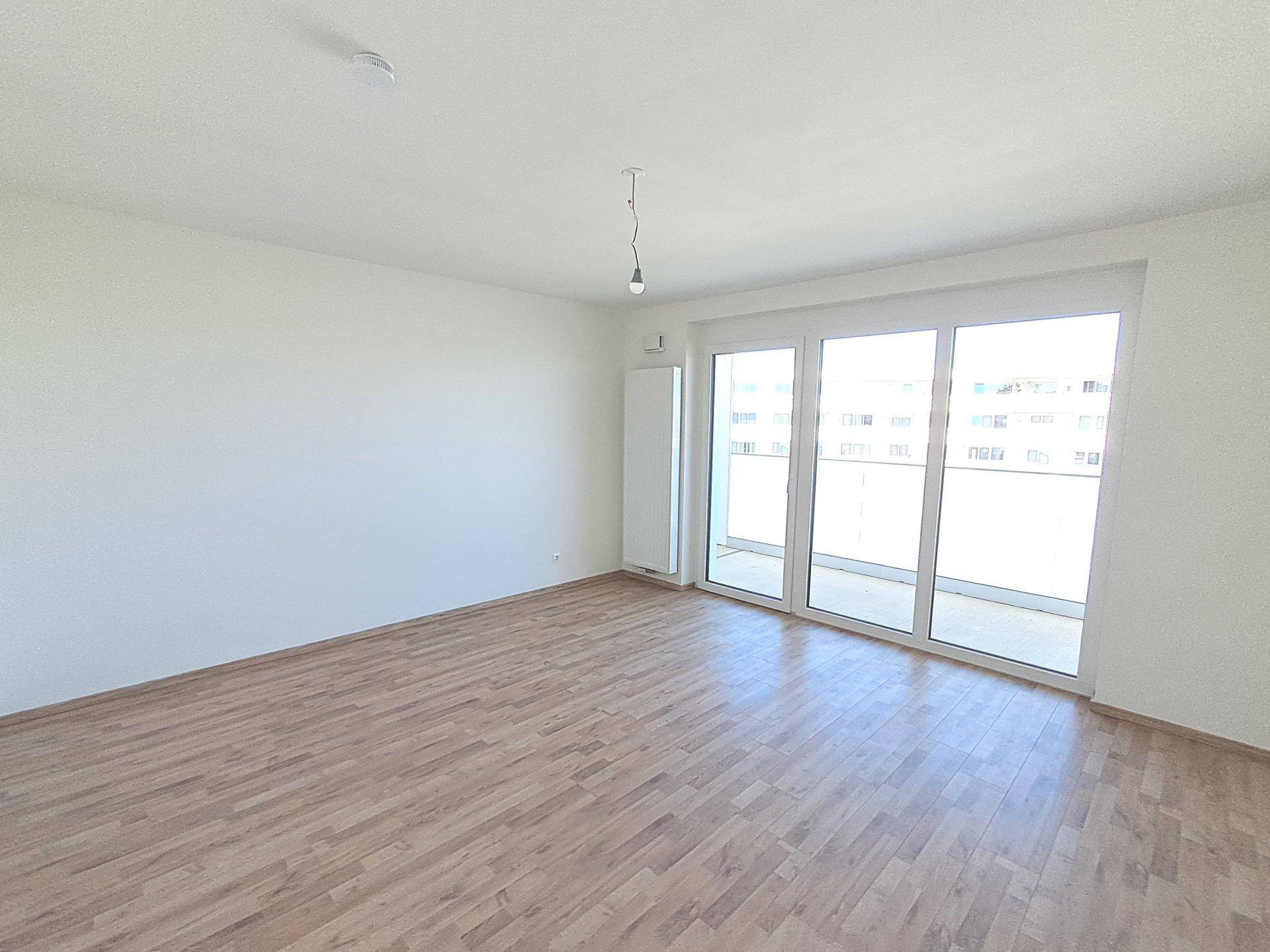 Heller Raum mit Laminatboden und breiter Fensterfront, die Zugang zum Balkon bietet.