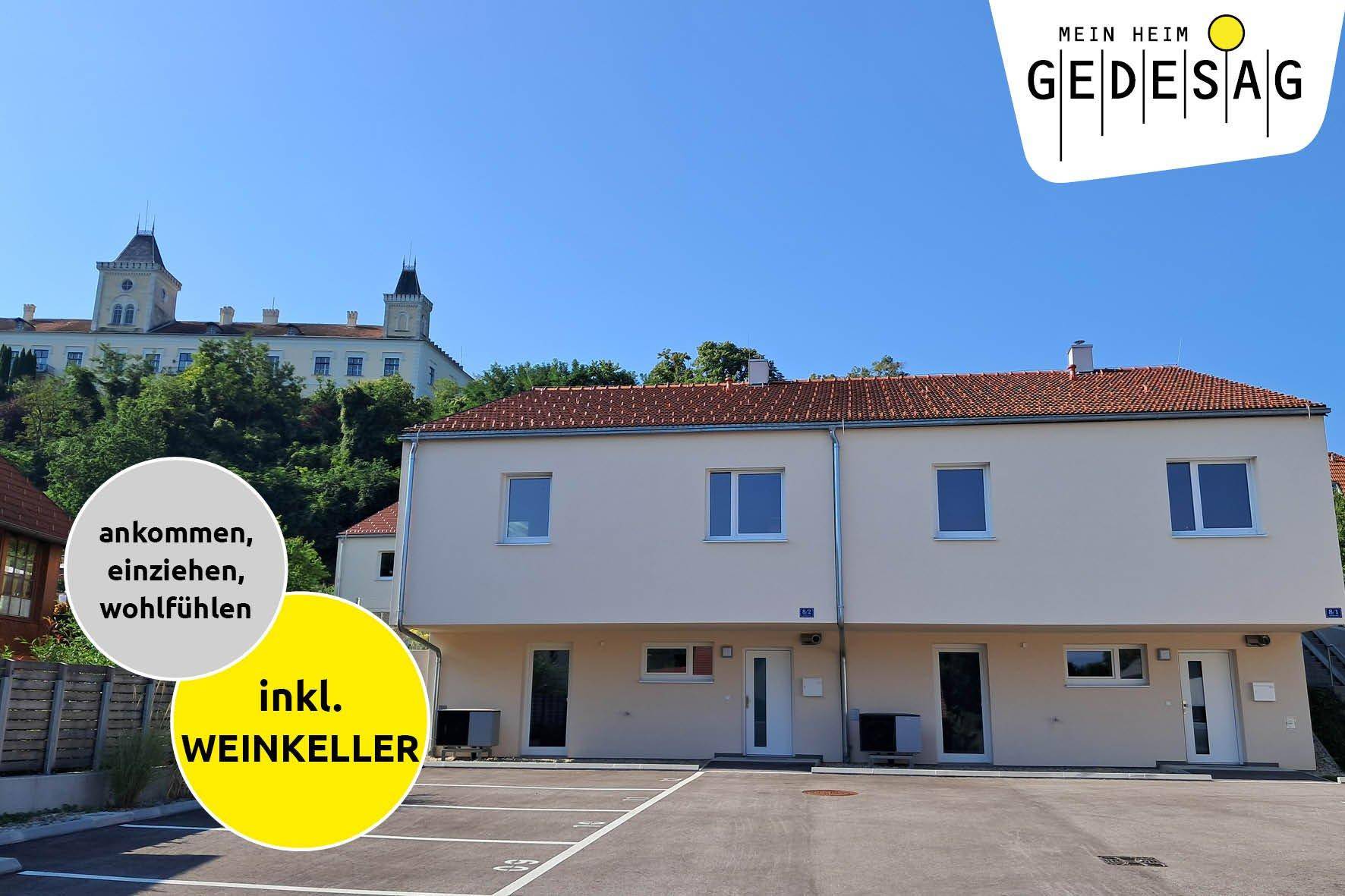 Außenansicht eines modernen Gebäudes mit Parkplätzen und einem historischen Schloss im Hintergrund.