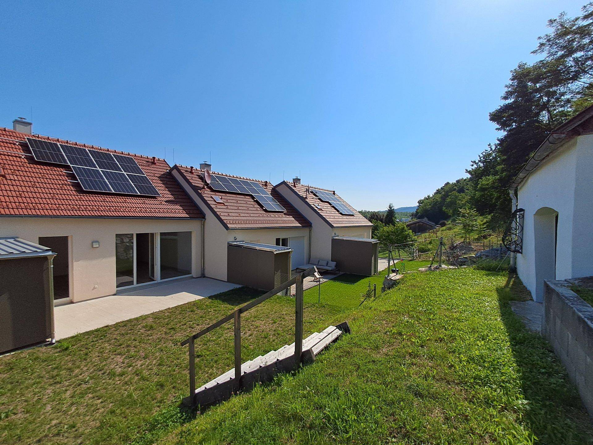 Reihenhäuser mit Solaranlagen und Terrassen, umgeben von einer grünen Hanglandschaft.