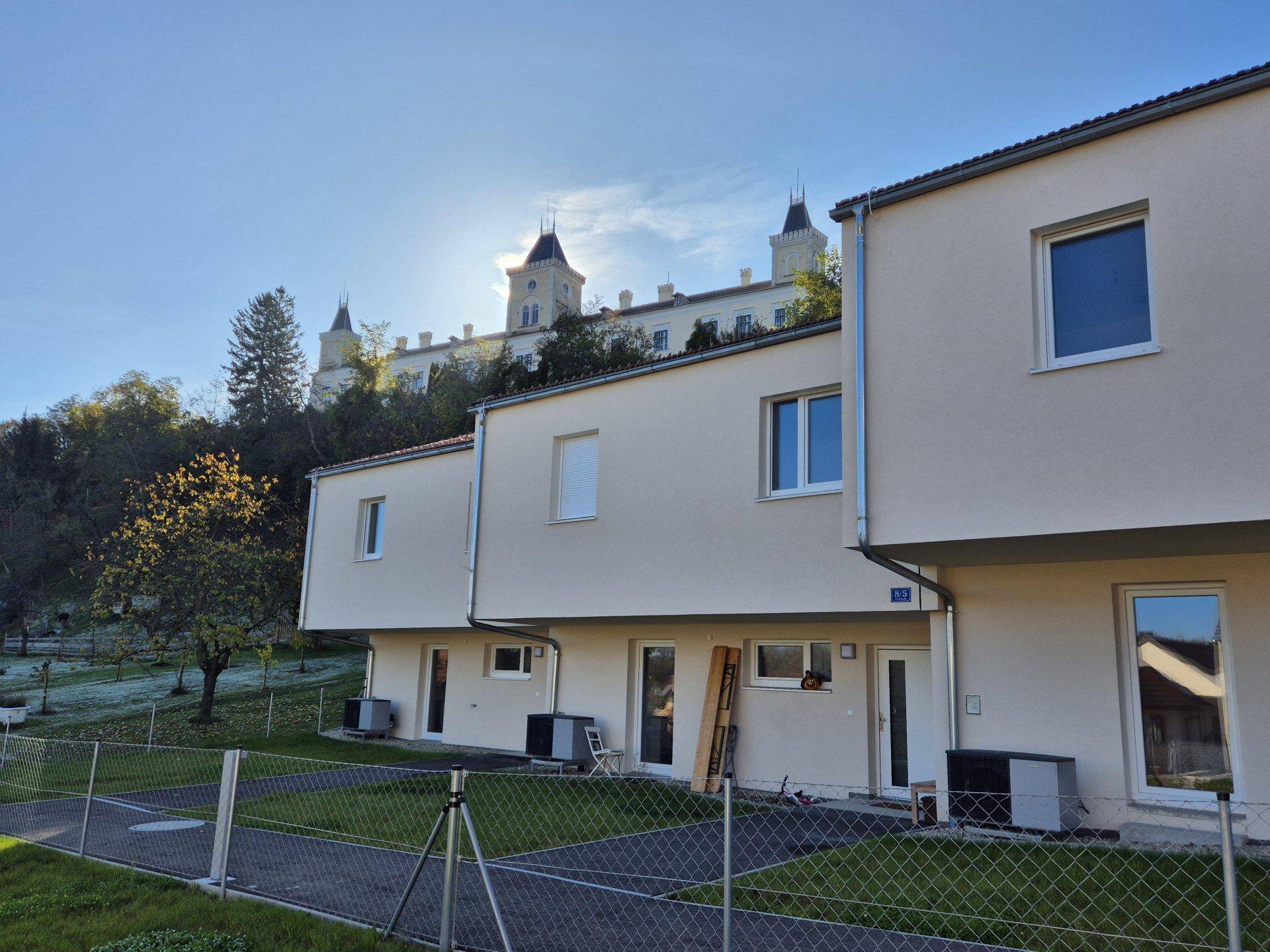 Moderne Reihenhäuser mit Blick auf ein historisches Schloss auf dem gegenüberliegenden Hügel.