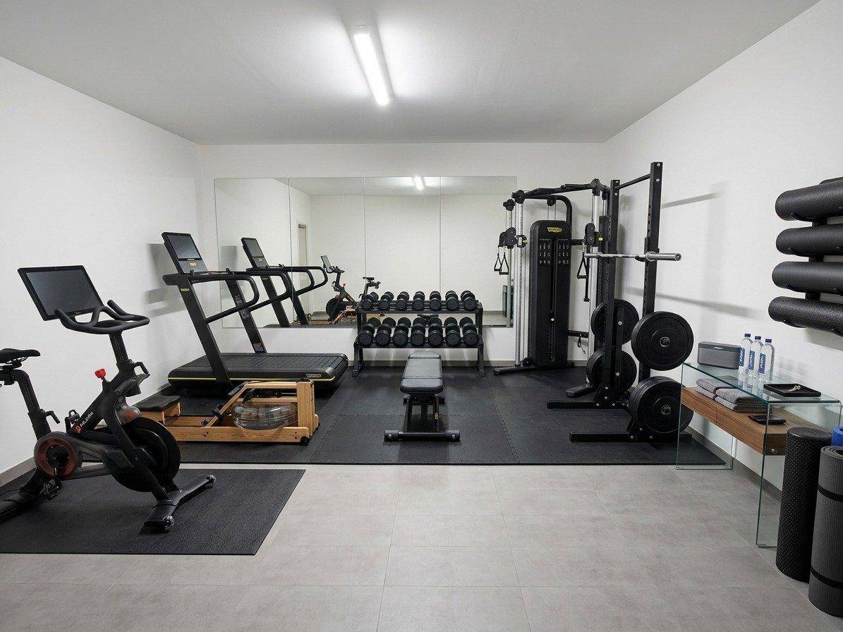 Gut ausgestatteter Fitnessraum mit verschiedenen Trainingsgeräten und einem großen Spiegel.