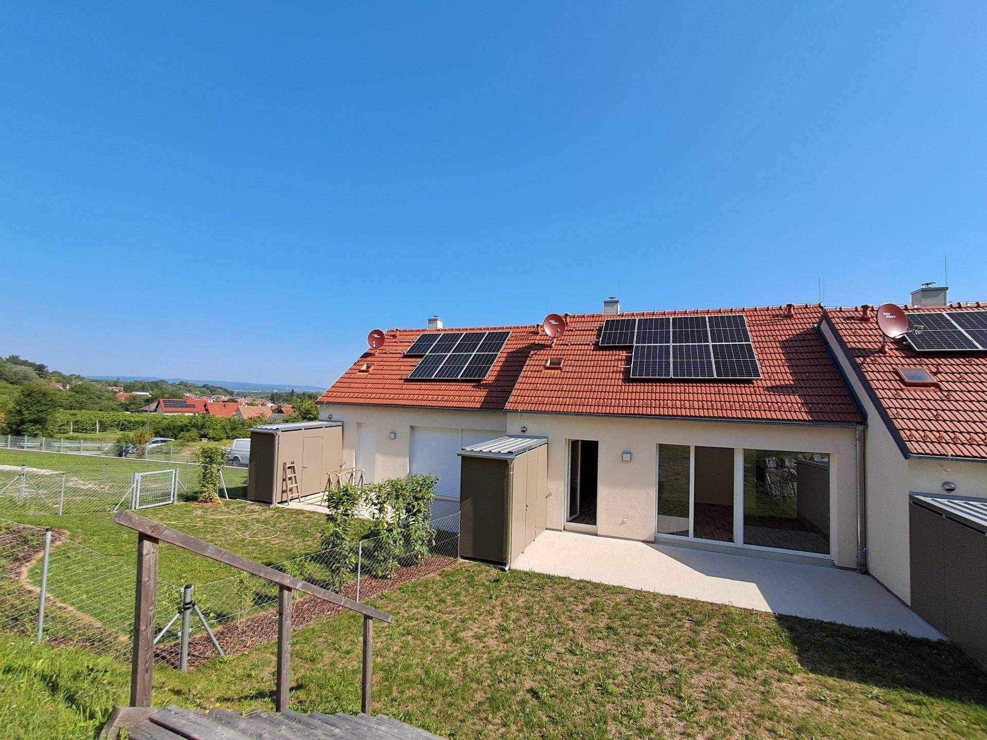 Rückansicht von Reihenhäusern mit Solaranlagen auf den Dächern und privaten Gärten.