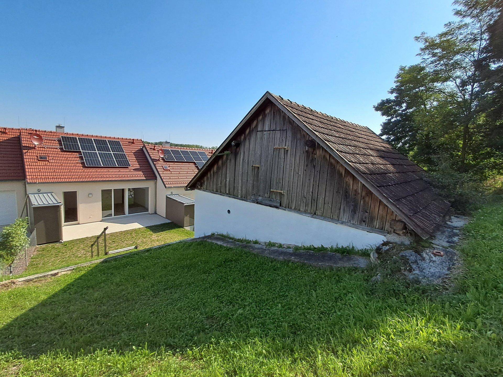 Rückseite der neuen Reihenhäuser mit Solaranlagen und einem traditionellen Holzschuppen.