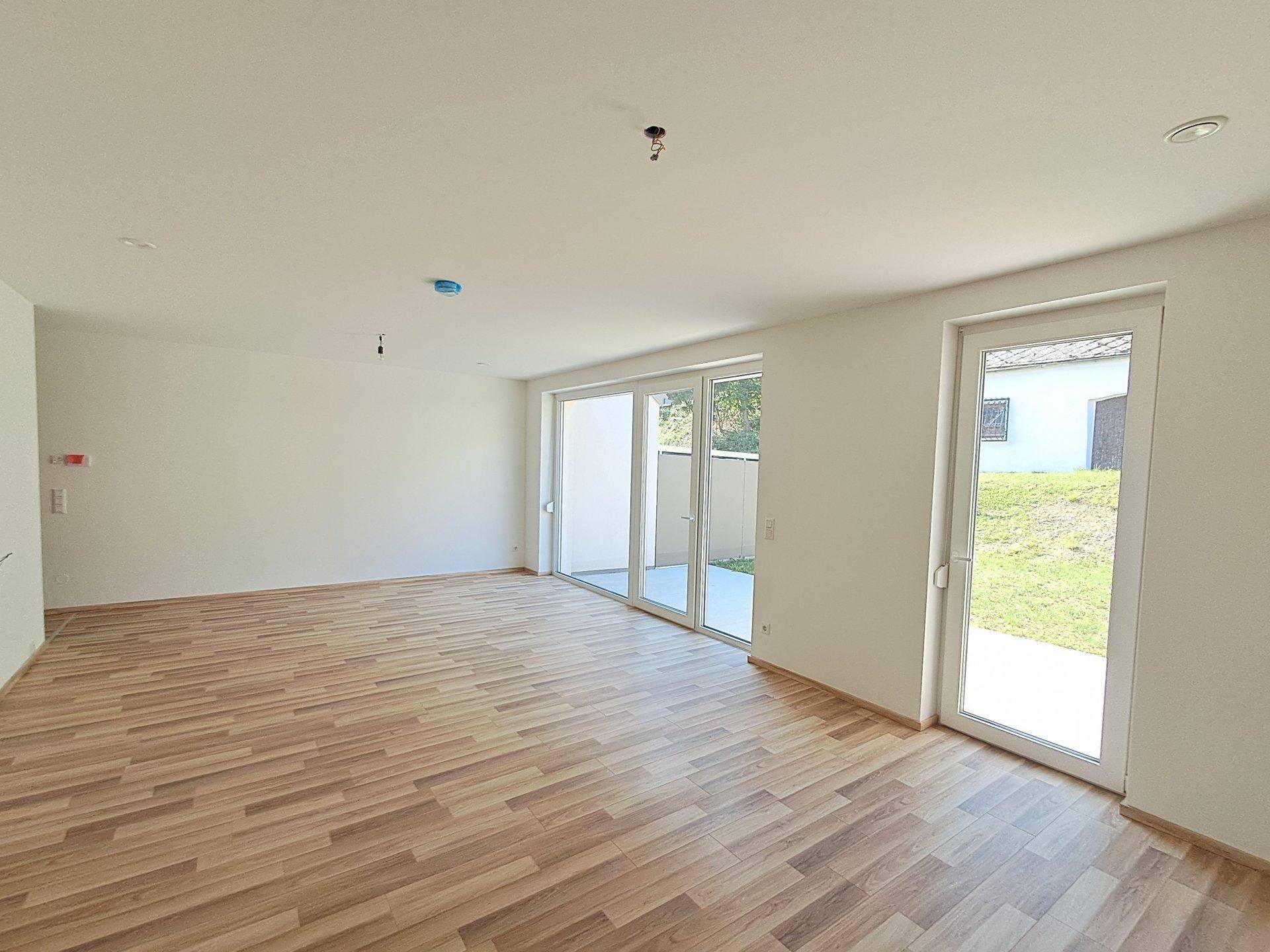 Geräumiger, unmöblierter Wohnraum mit Holzfußboden und großen Fenstern, bereit zum Einzug.