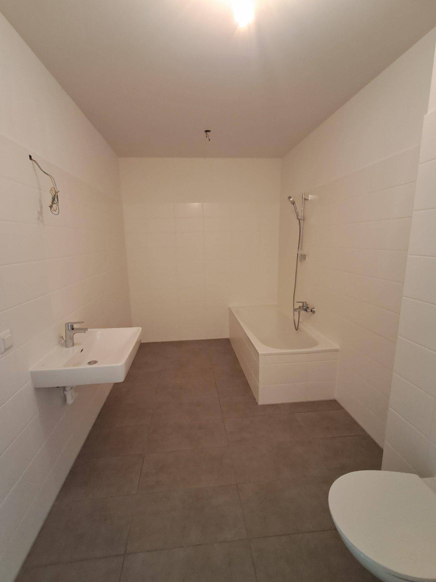 Unfertiges Badezimmer mit Badewanne, Waschbecken und Toilette, bereit für den letzten Ausbau.