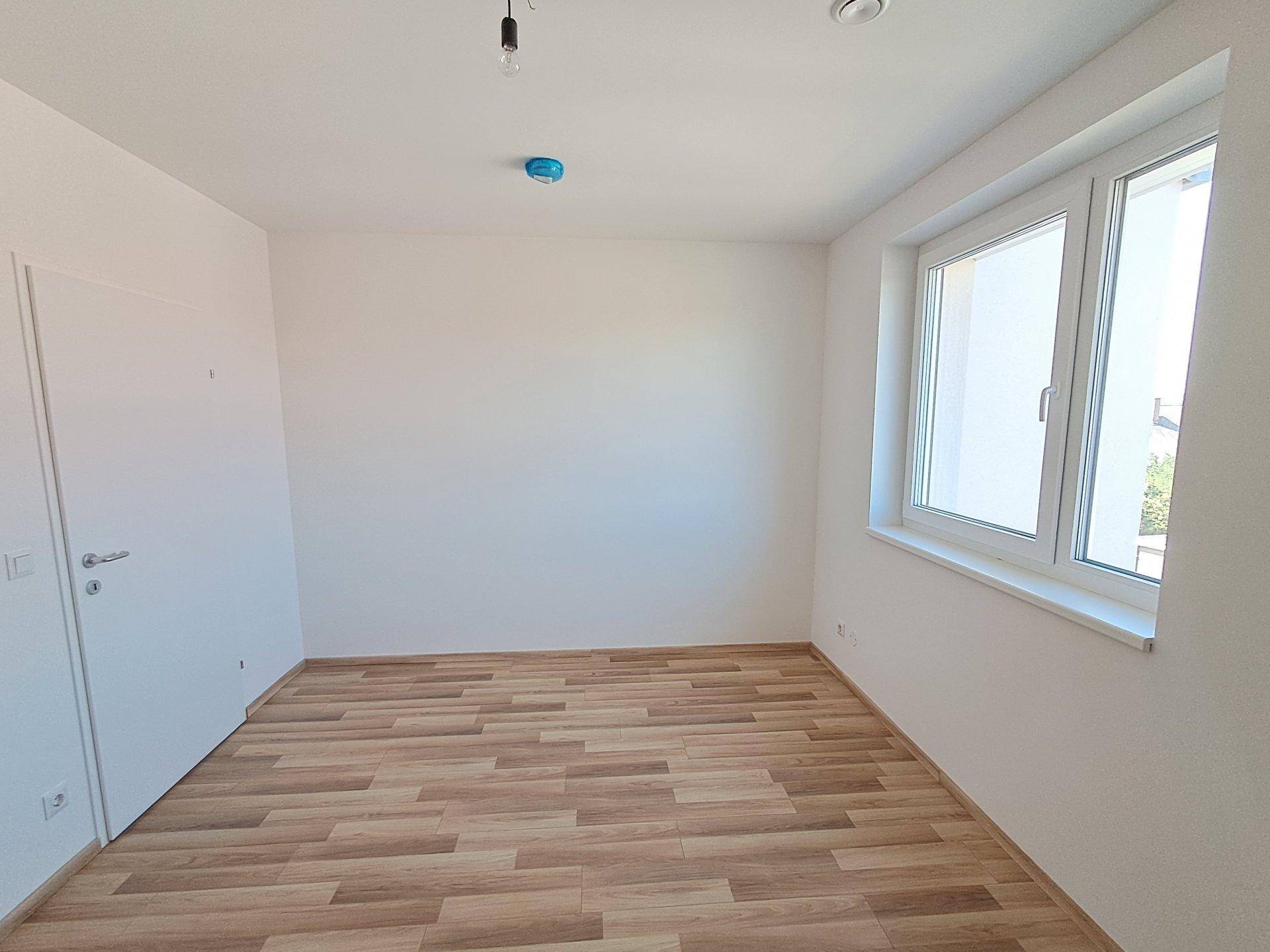 Leeres Zimmer mit Holzfußboden und einem großen Fenster, ideal als Schlaf- oder Arbeitszimmer.