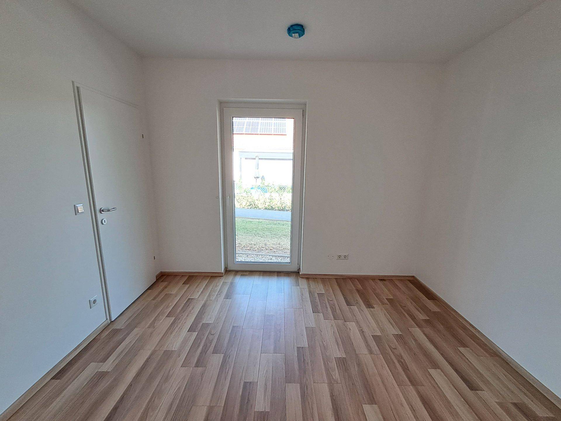 Leerer Raum mit Laminatboden und Zugang zu einem kleinen Gartenbereich.