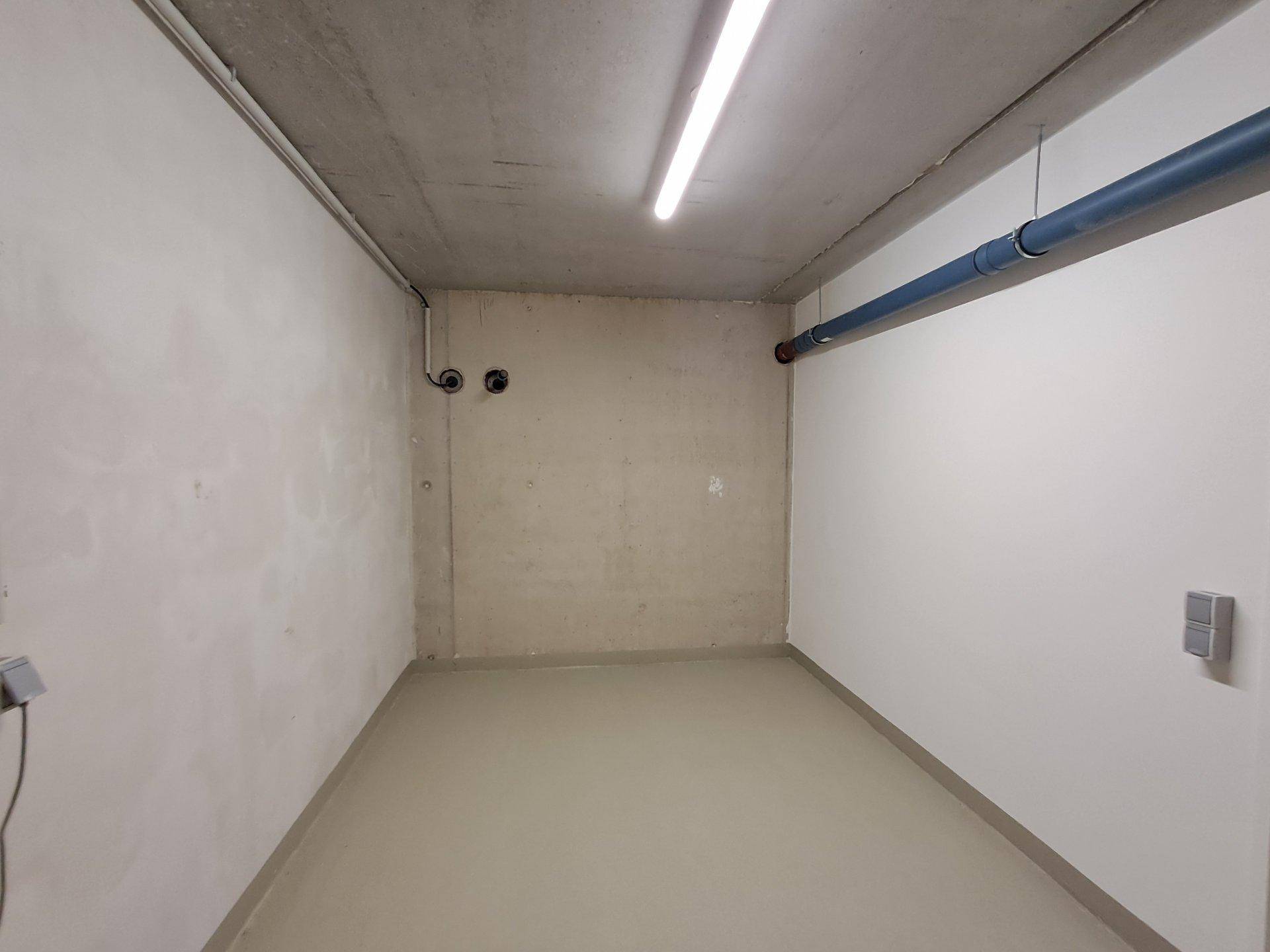 Leerer Abstellraum im Keller mit Betonwänden und sichtbaren Leitungen.