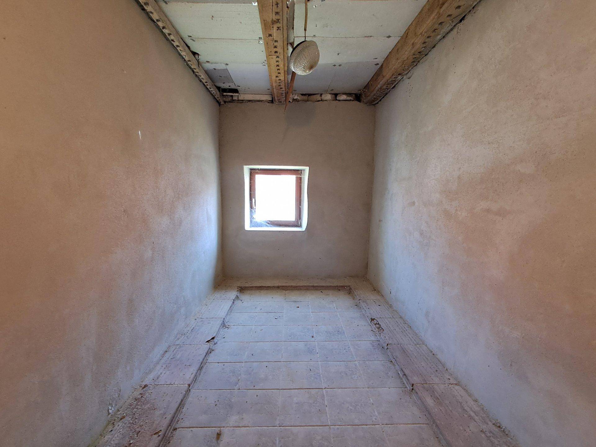 Kleiner, unfertiger Raum mit einem Fenster und sichtbaren Holzbalken an der Decke.