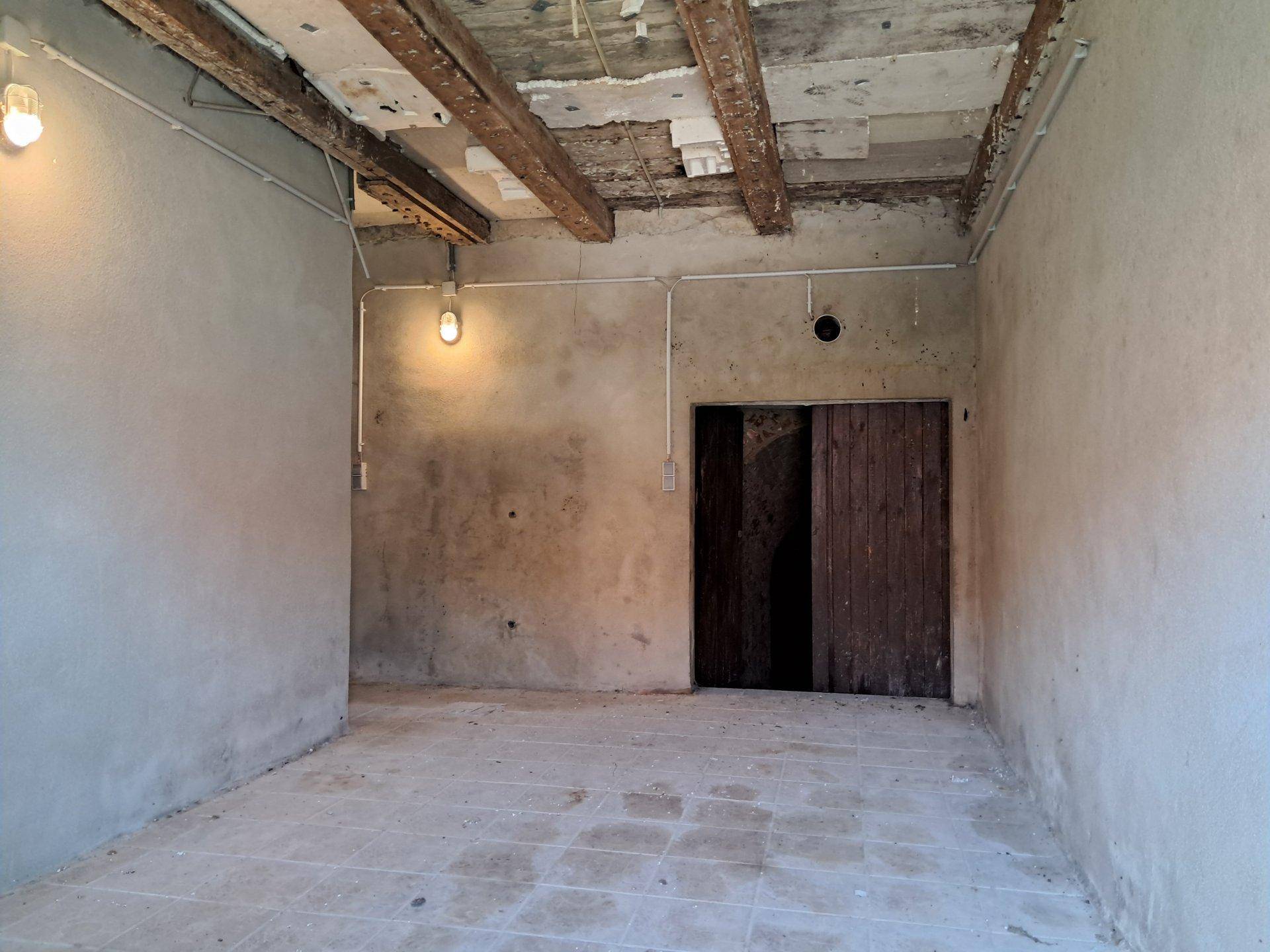 Unfertiger Raum mit sichtbaren Holzbalken, Betonboden und einer alten Holztür.
