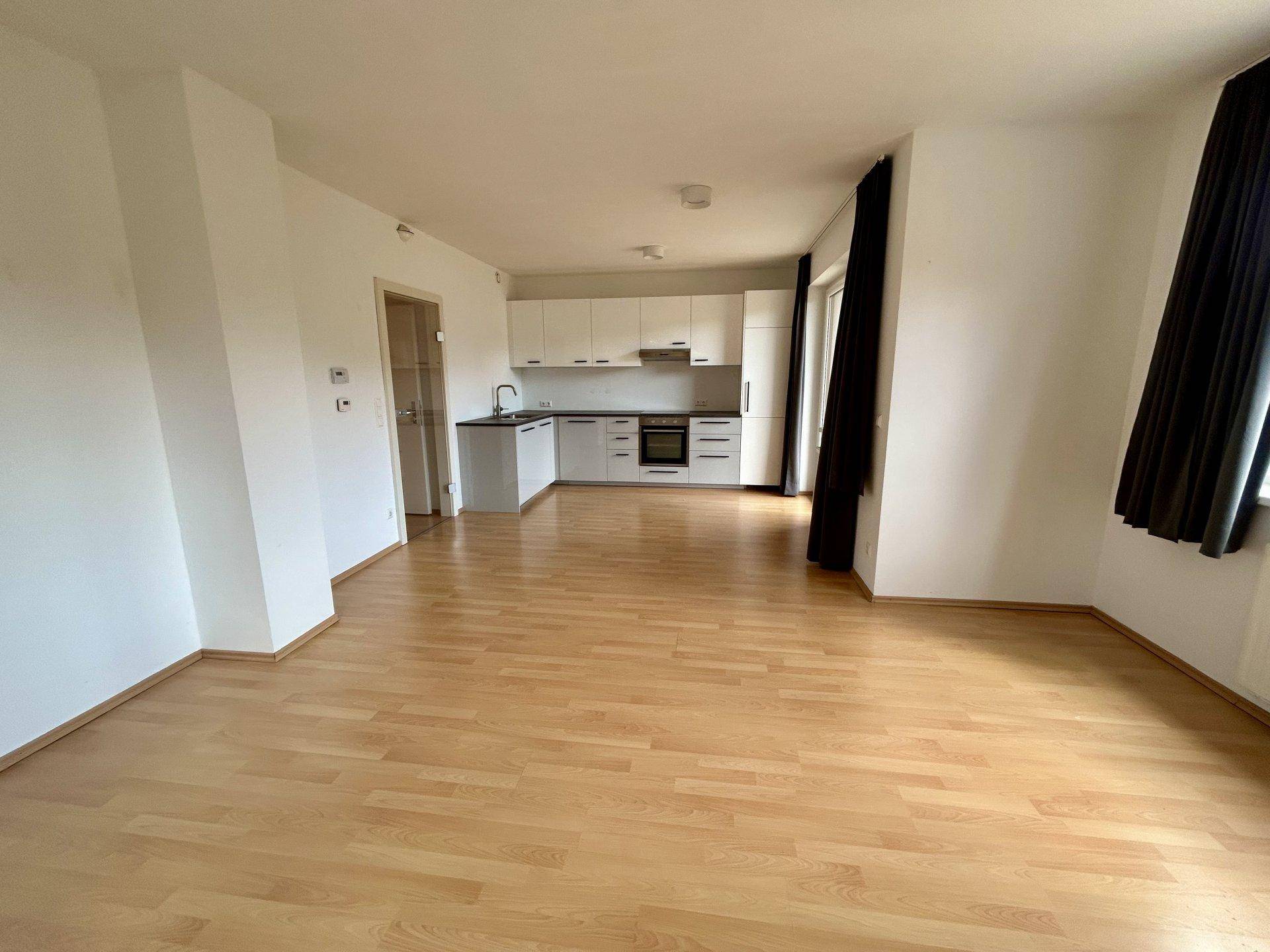 Offener Wohnbereich mit integrierter Küche, hellem Laminatboden und viel Tageslicht.
