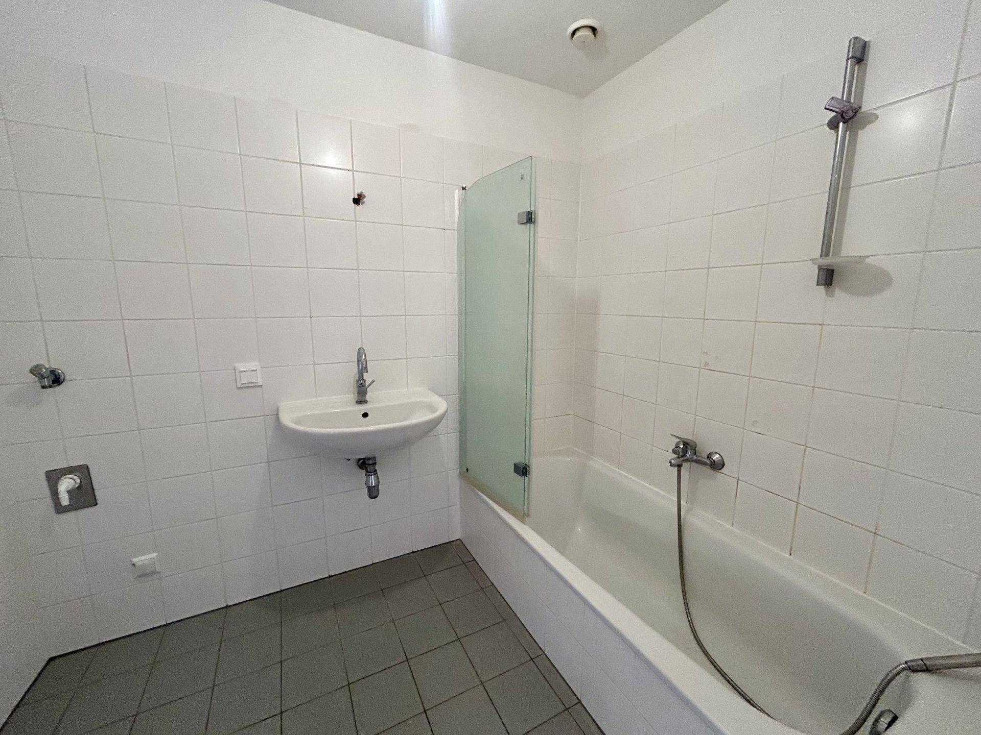 Badezimmer mit weißen Fliesen, Badewanne und Waschbecken, ausgestattet mit einer Duschabtrennung.