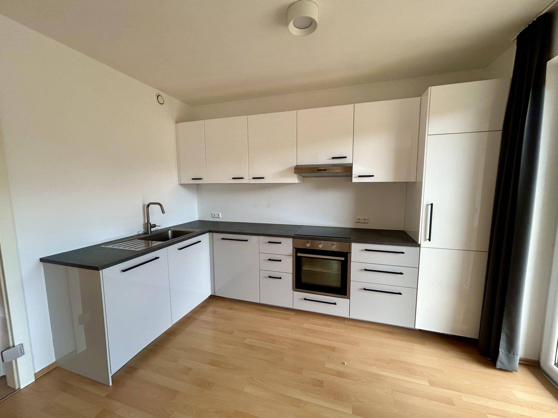 Moderne Einbauküche mit weißen Hochglanzfronten, dunkler Arbeitsplatte und integrierten Geräten.