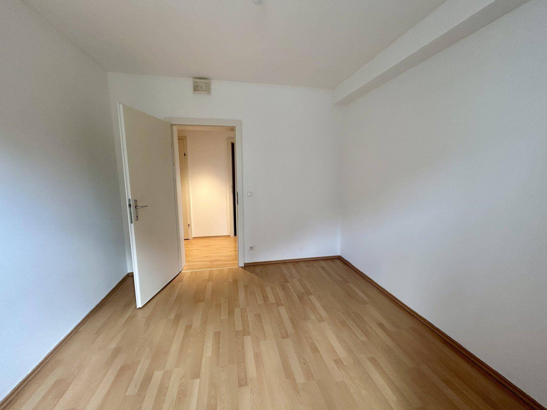 Helles Schlafzimmer mit Laminatboden und weiß gestrichenen Wänden, bereit zur individuellen Gestaltung.
