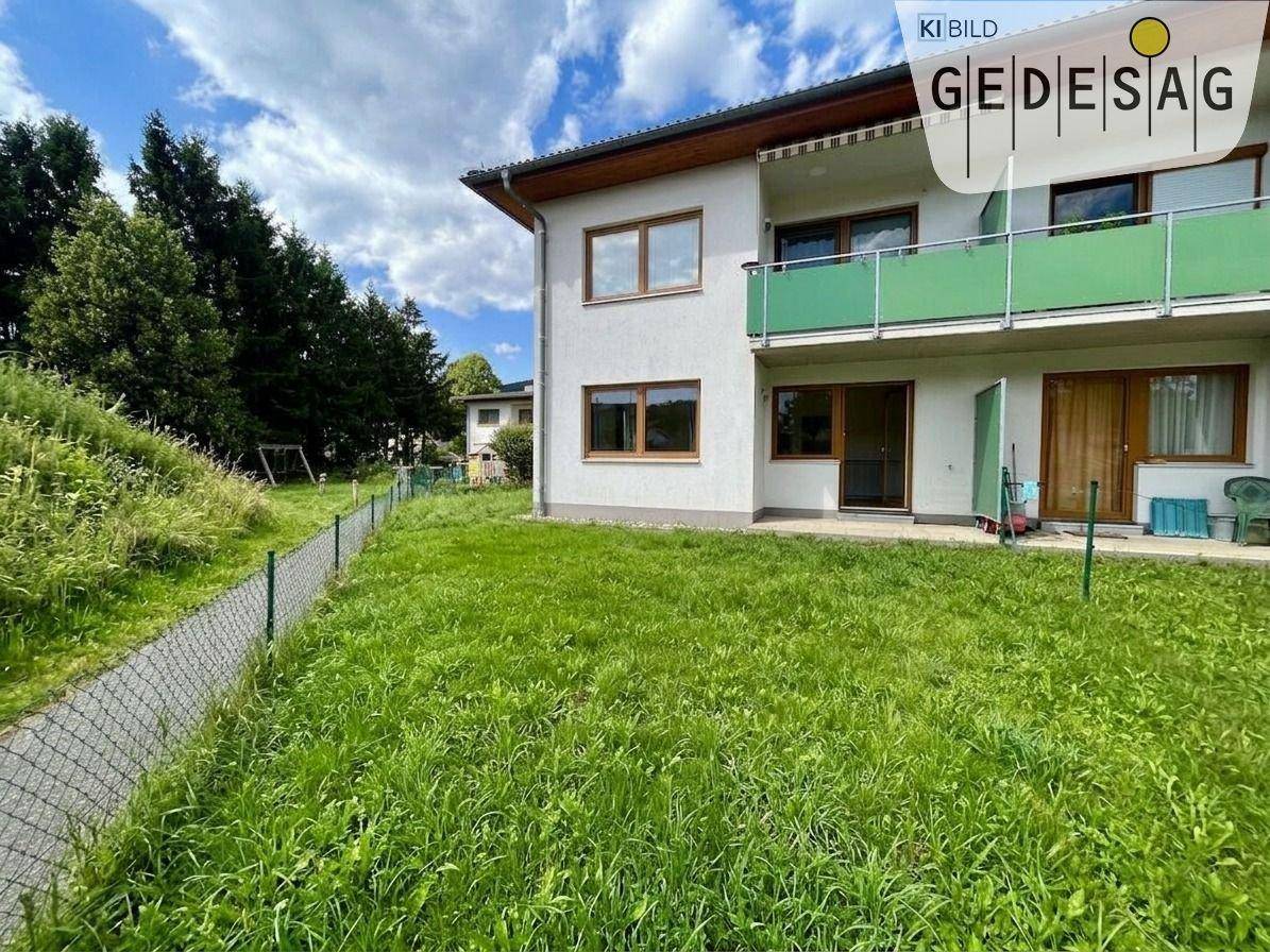 Gebäudeseite mit Balkon und angrenzendem Gartenbereich, umgeben von hohen Bäumen.