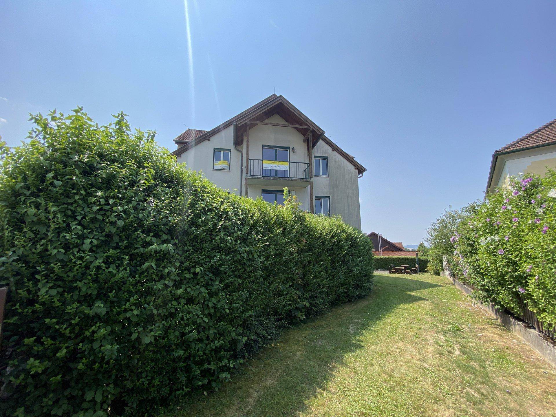 Seitenansicht des Gebäudes, teilweise von einer hohen Hecke verdeckt, mit kleinem Balkon.