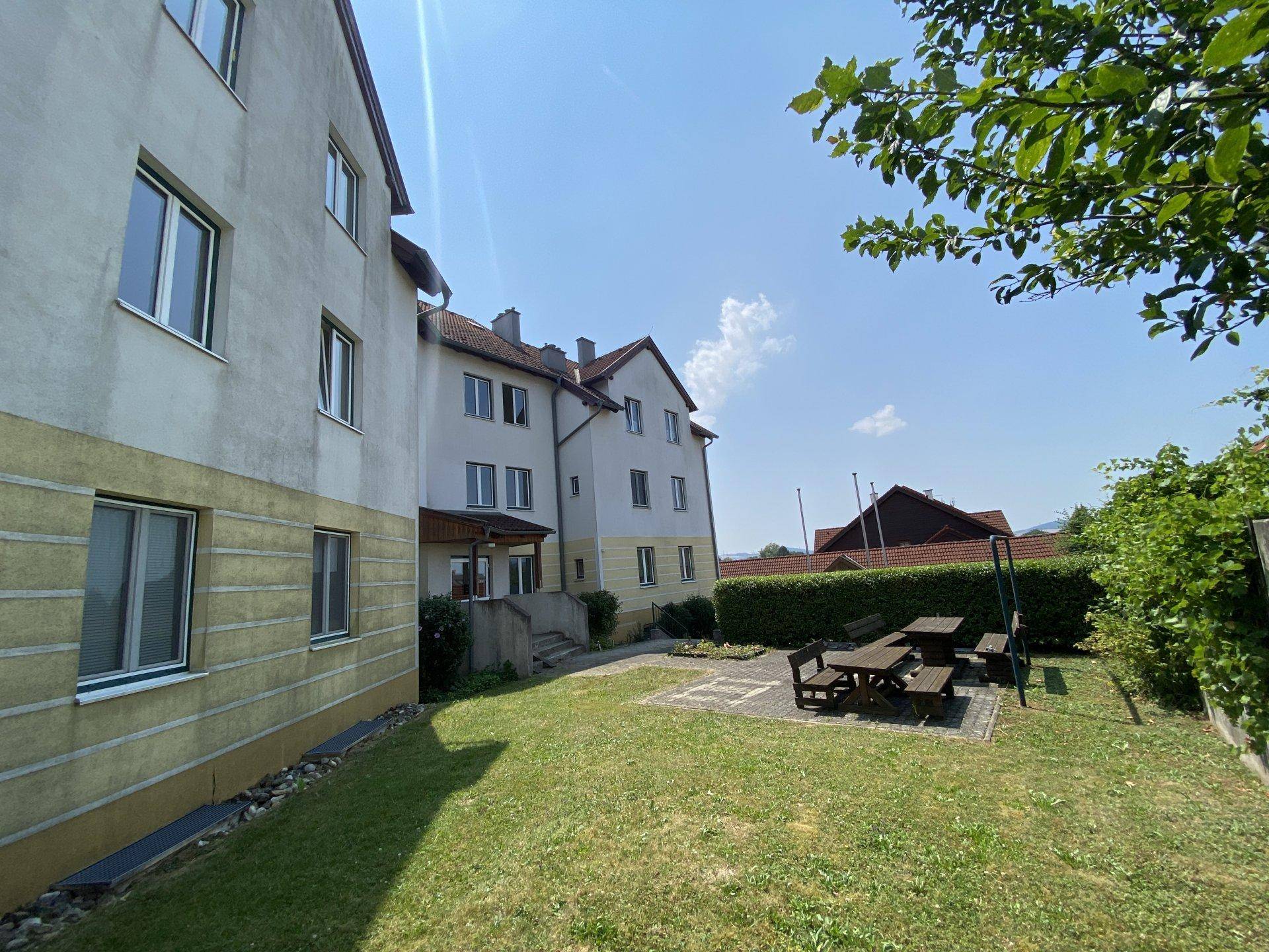 Seitenansicht des Gebäudes mit großer Rasenfläche und Picknicktischen im Freien.