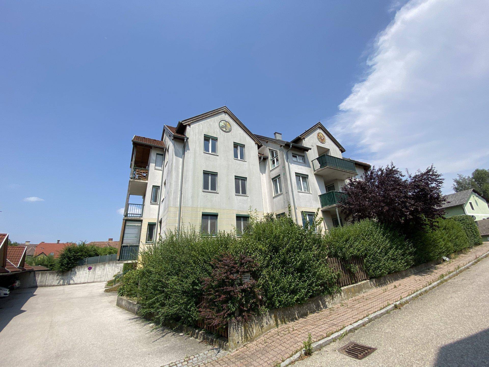 Mehrfamilienhaus mit Balkonen und einem gepflasterten Parkplatzbereich im Vordergrund.