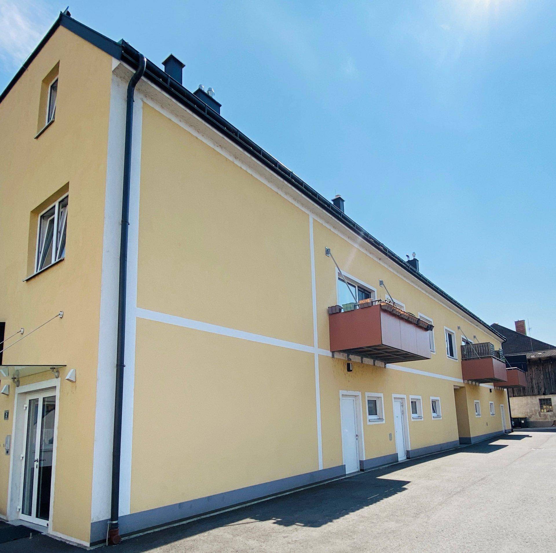 Lange gelbe Fassade eines Wohnhauses mit Balkonen und Eingangsbereichen unter strahlend blauem Himmel.