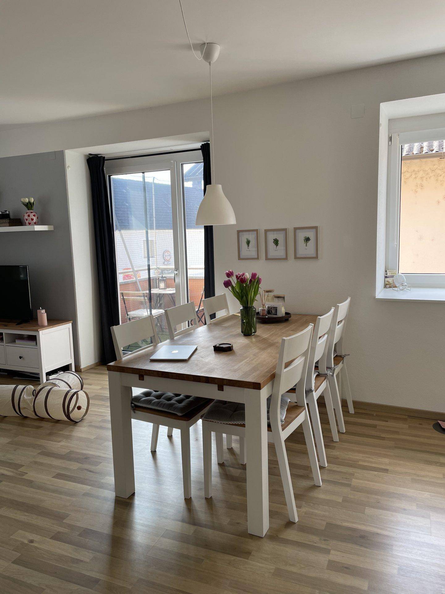 Heller Essbereich mit Holztisch, weißen Stühlen und Zugang zu einem Balkon.