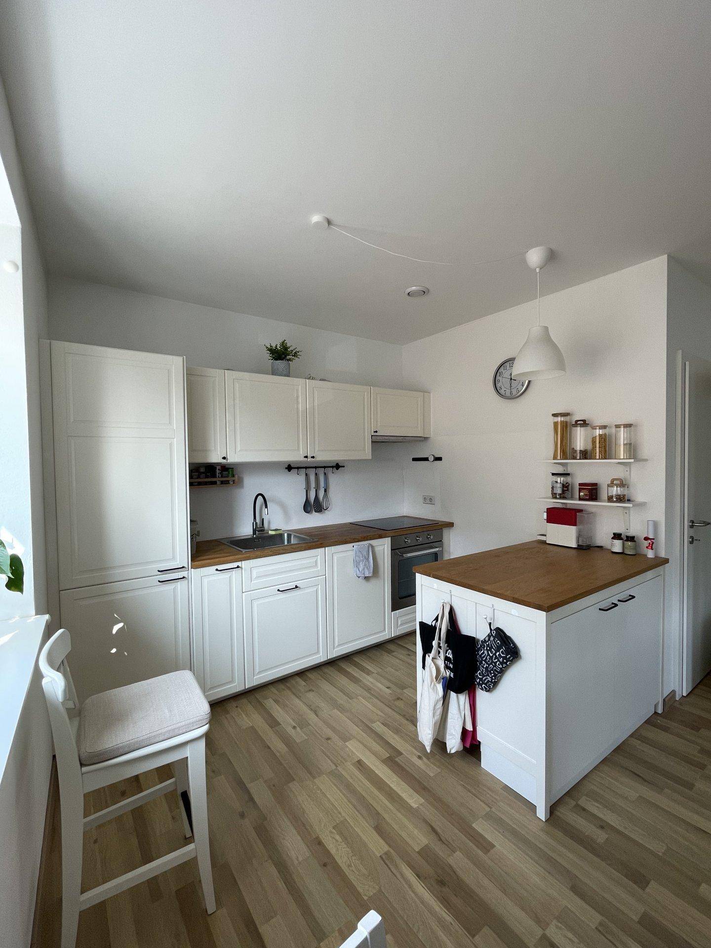Helle, moderne Küche mit weißen Schränken, Holztheke und integrierter Kücheninsel.