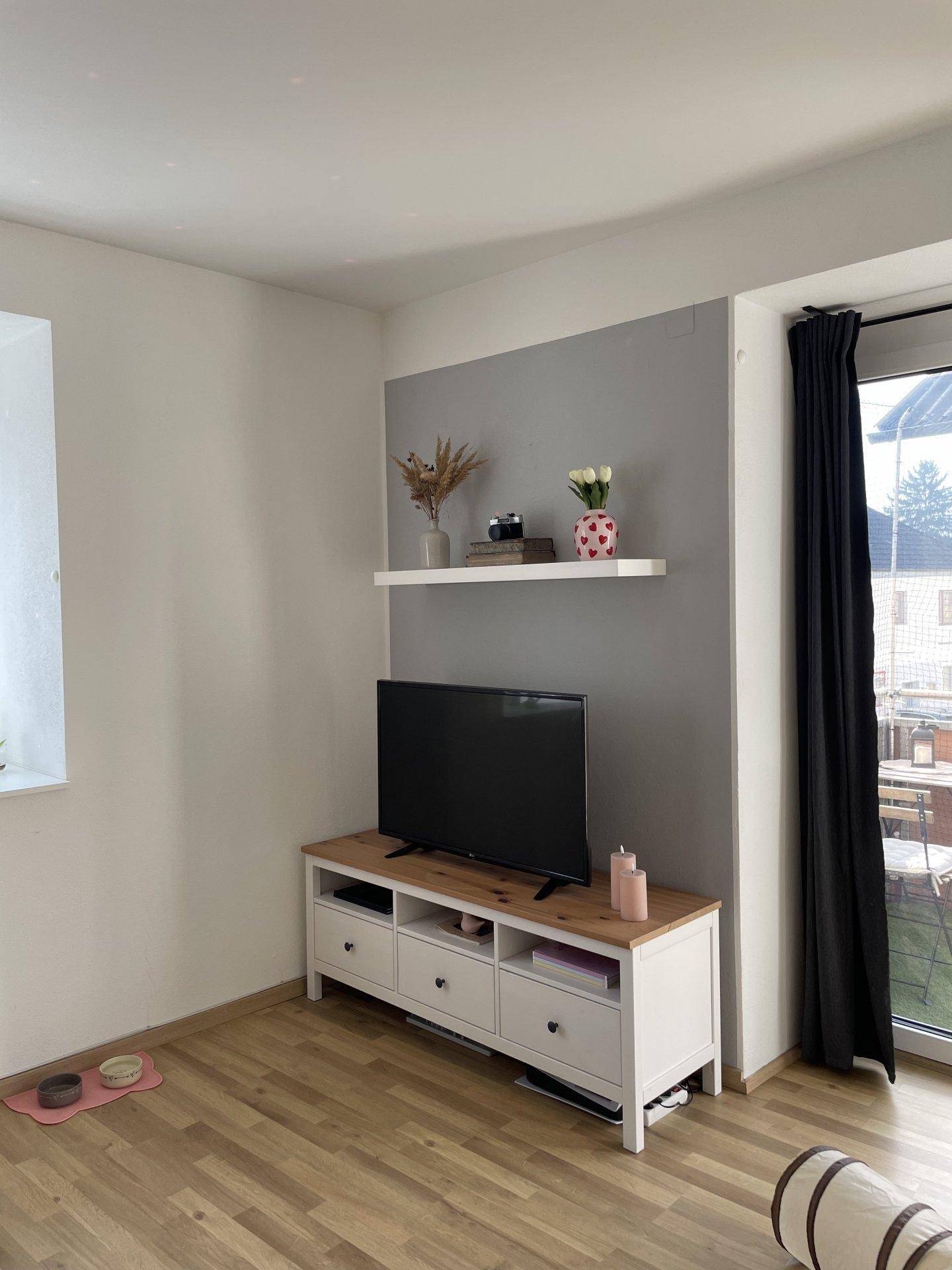 Moderner Wohnbereich mit TV-Möbel, Wandregal und Zugang zu einem Außenbereich.