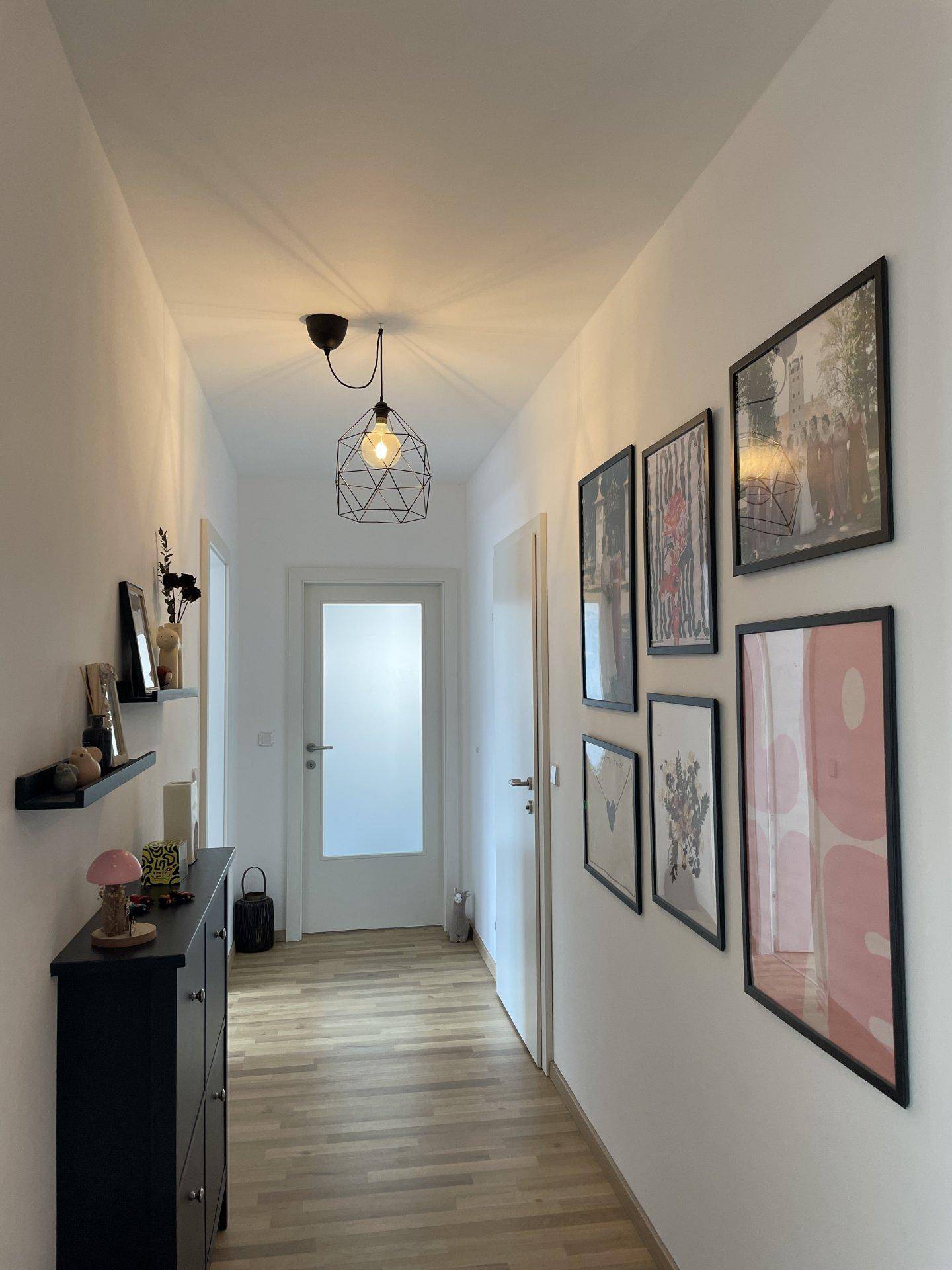 Heller Flur mit Laminatboden, modernen Bildern an der Wand und stilvoller Beleuchtung.
