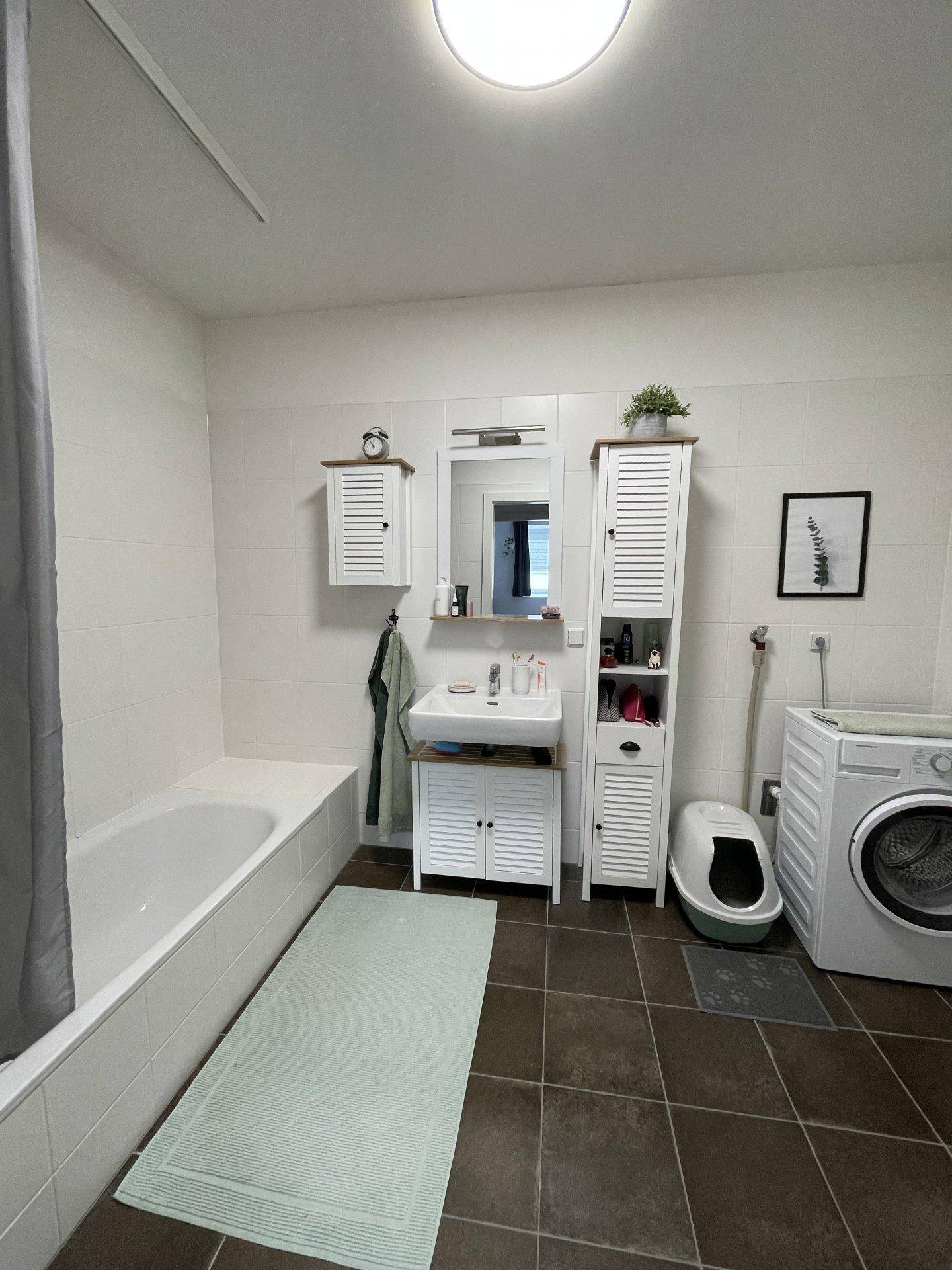 Modernes Badezimmer mit Badewanne, Waschbecken und Waschmaschine, in hellen Fliesen gehalten.
