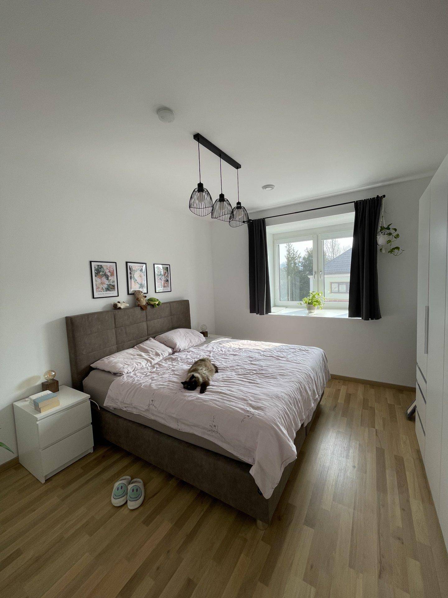 Helles Schlafzimmer mit Doppelbett, Nachttischen und großem Fenster mit Blick ins Grüne.