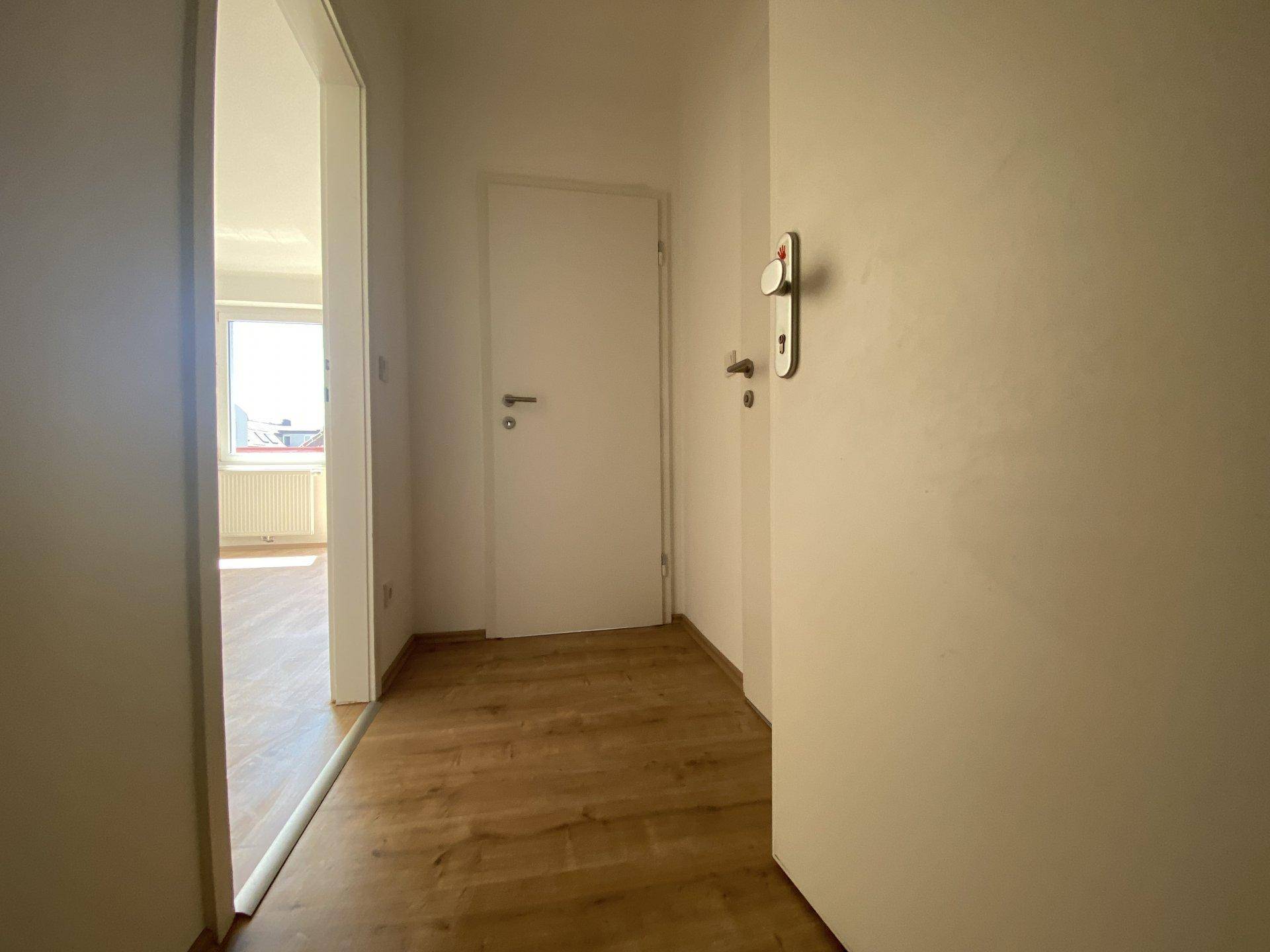 Heller Flur mit Holzboden und weiß gestrichenen Wänden, der zu weiteren Räumen führt.