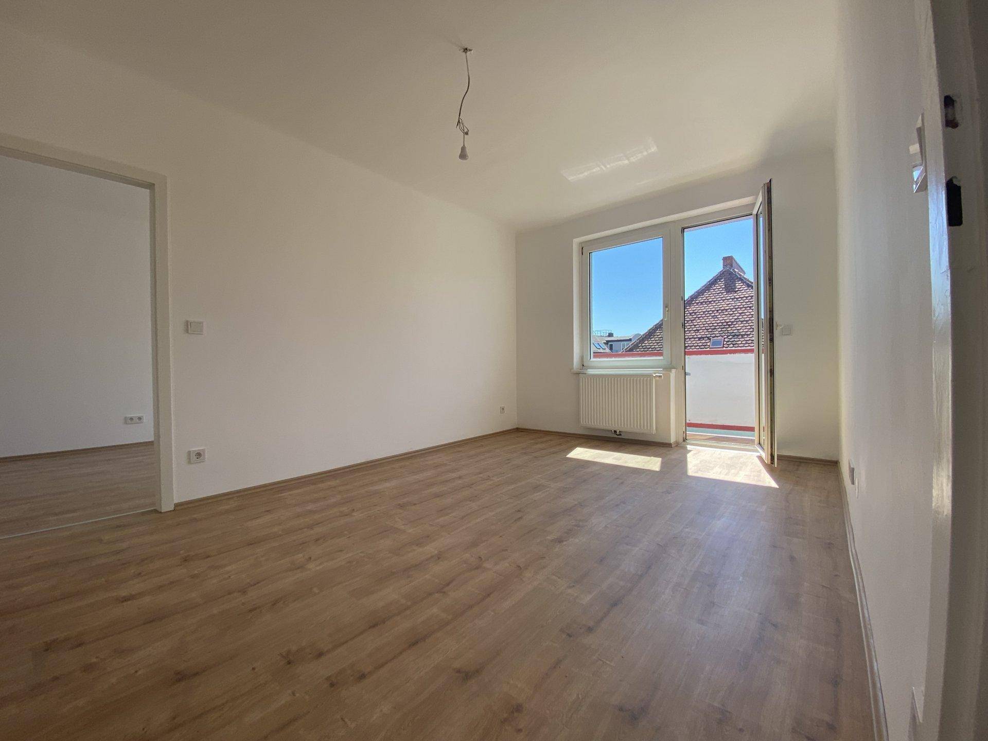 Geräumiger, heller Raum mit Holzboden und direktem Zugang zu einem Balkon oder einer Terrasse.