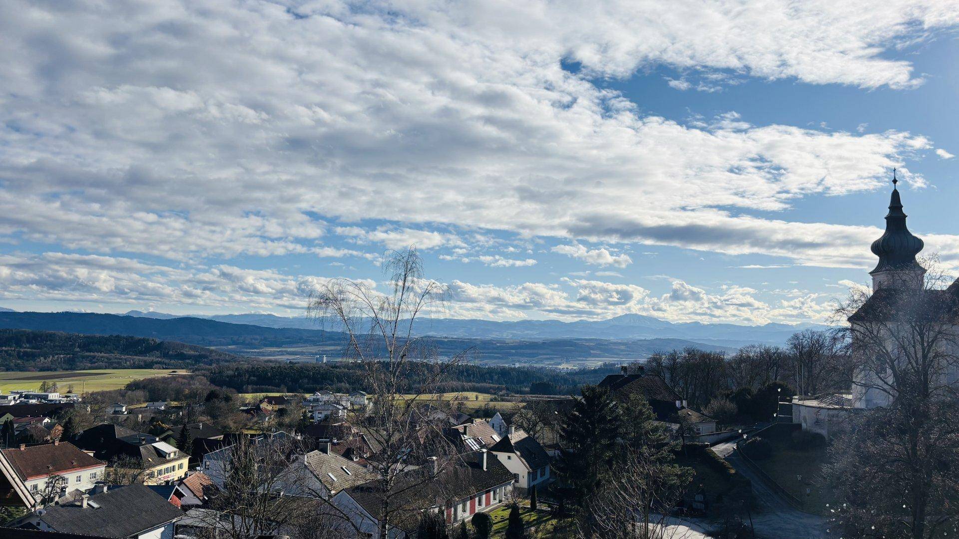 Weitläufiger Panoramablick über eine Stadt mit Bergen im Hintergrund unter einem blauen Himmel.