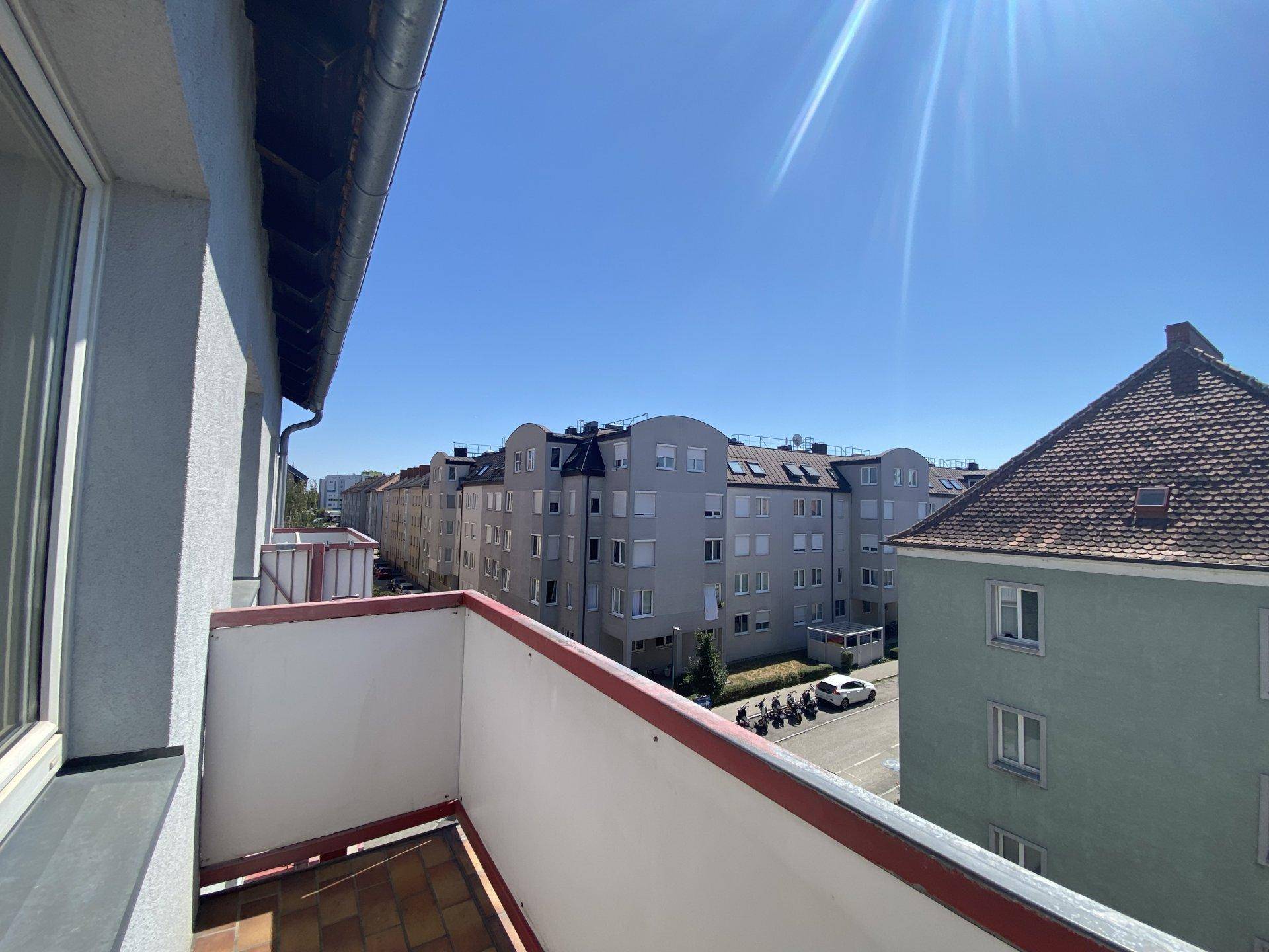 Balkon mit Blick auf die umliegenden Wohngebäude und die darunterliegende Straße an einem sonnigen Tag.