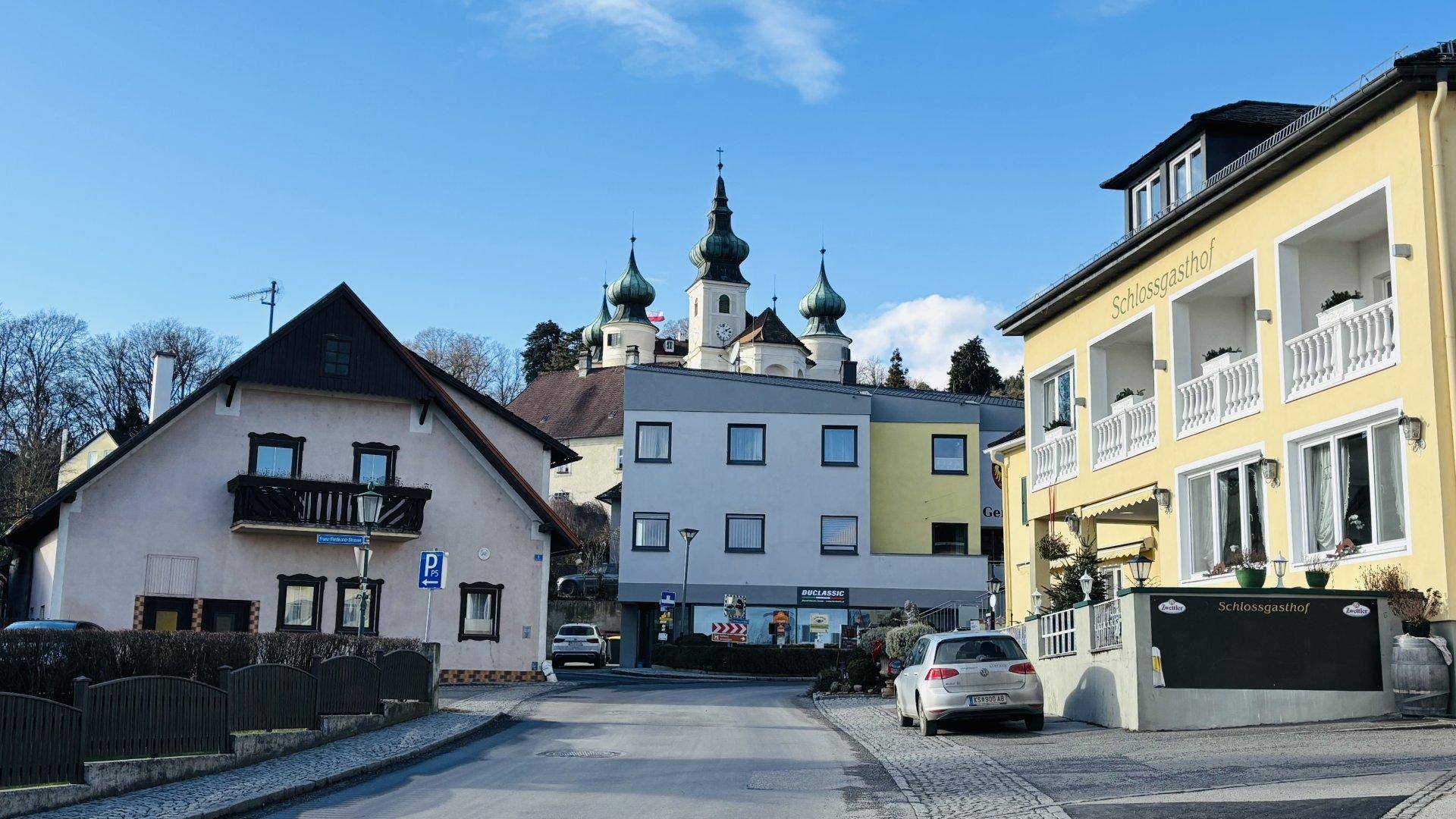 Straße in einer kleinen Stadt mit verschiedenen Gebäuden und einer Kirche im Hintergrund.