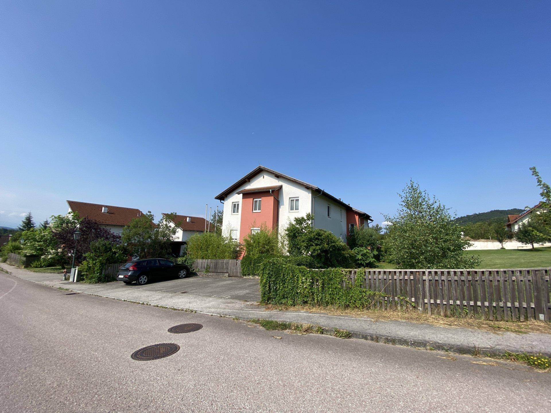 Wohnhaus mit großem Rasengrundstück und Holzzaun unter klarem, blauem Himmel.