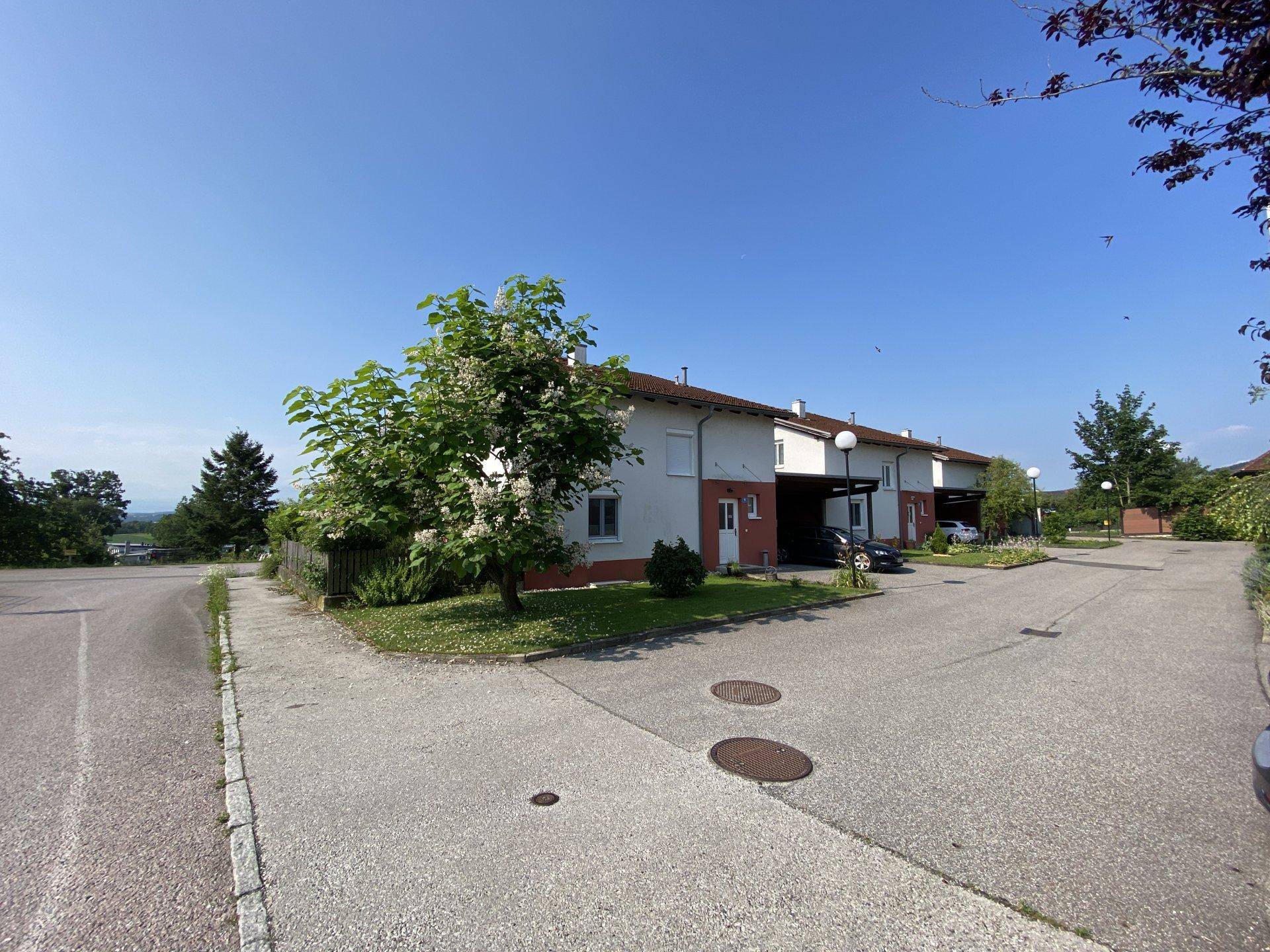 Reihe von Wohnhäusern mit Carports und gepflegter Außenanlage unter blauem Himmel.