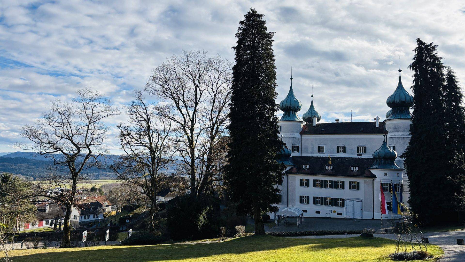 Historisches Schlossgebäude mit markanten Türmen und weitläufiger Parkanlage unter bewölktem Himmel.