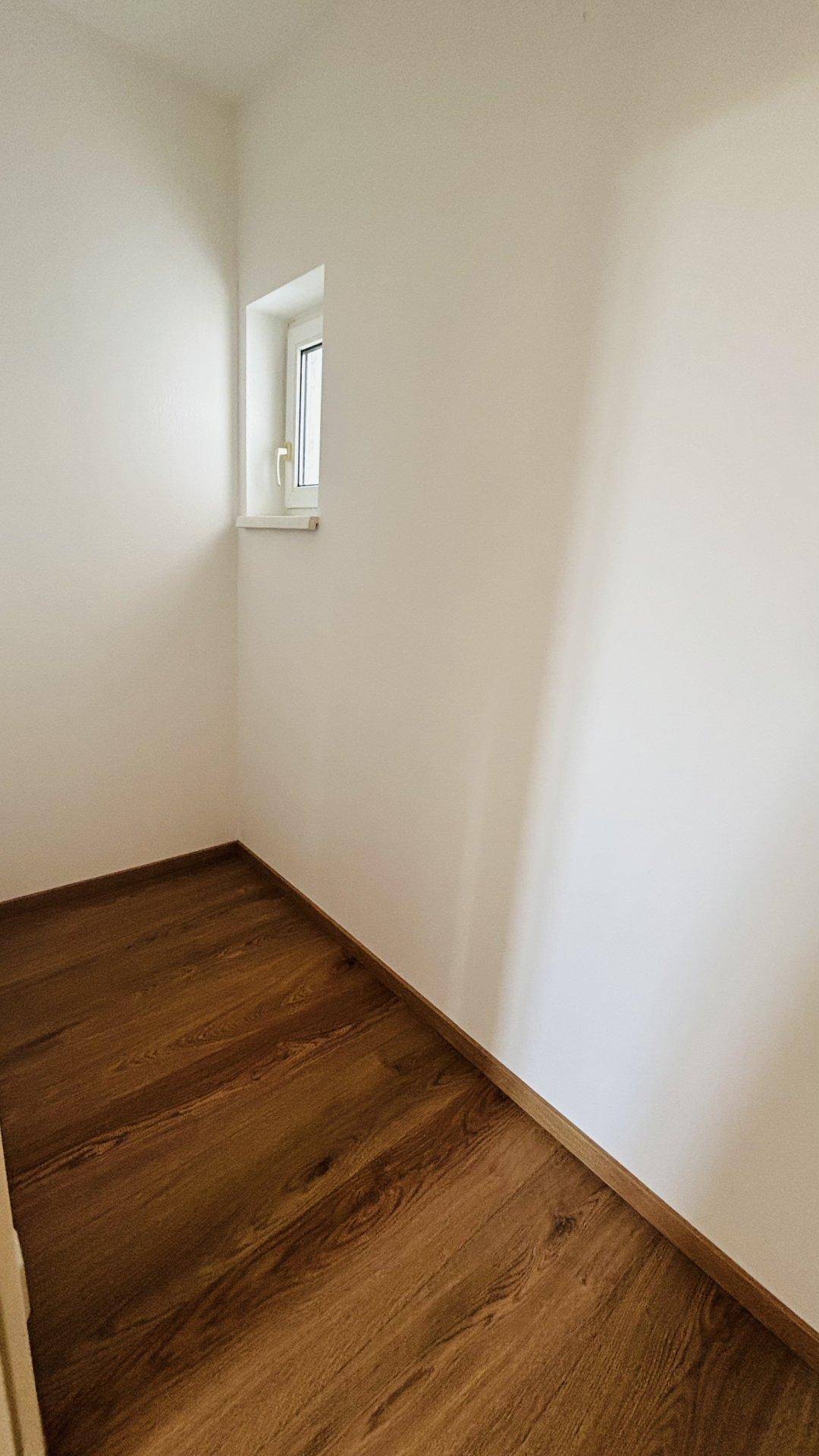 Kleiner, heller Raum mit Holzfußboden und einem Fenster, ideal als Abstellraum oder kleines Büro.