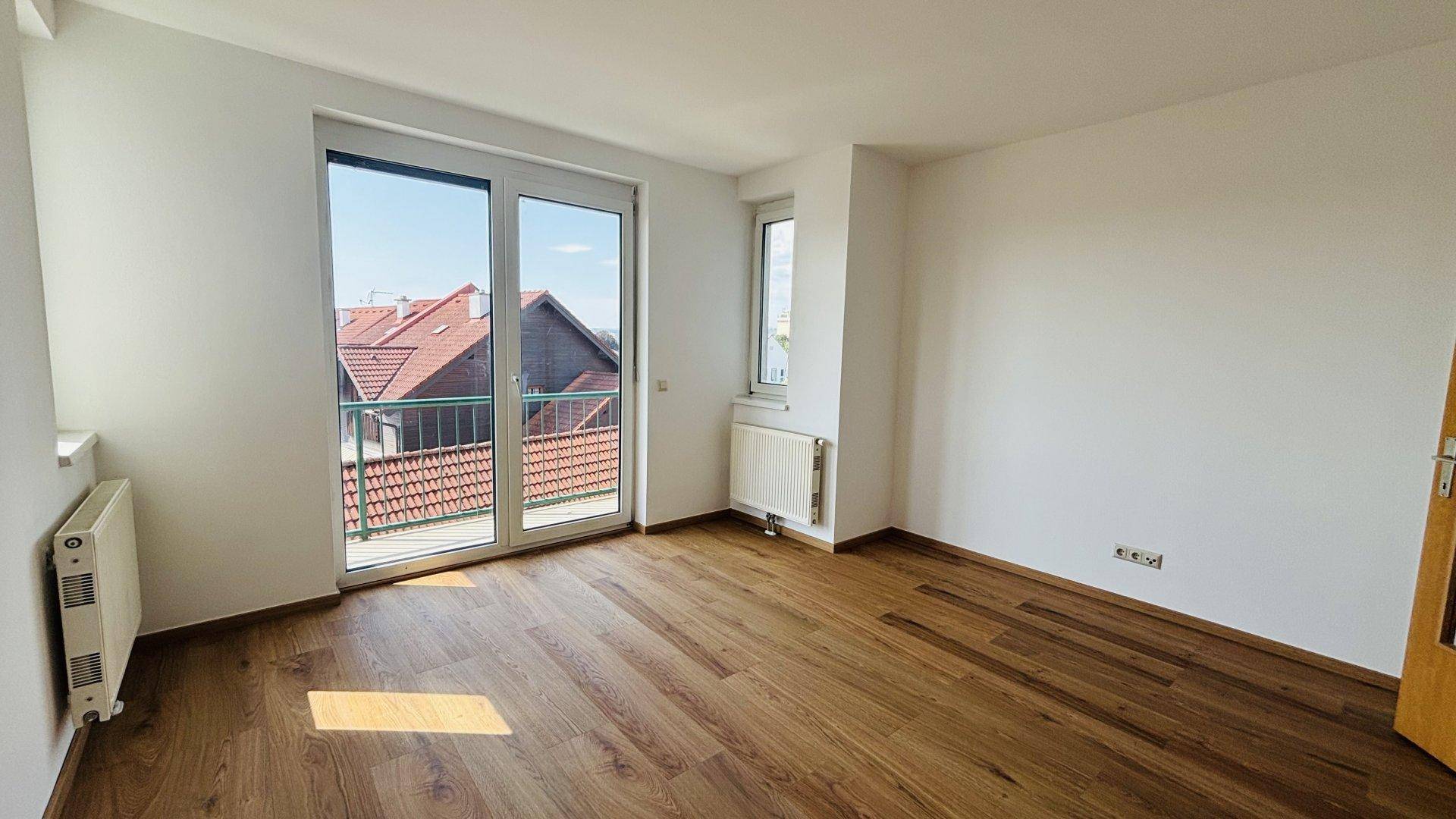 Helles Zimmer mit Holzfußboden und großem Balkonzugang, der viel Licht und eine Aussicht bietet.