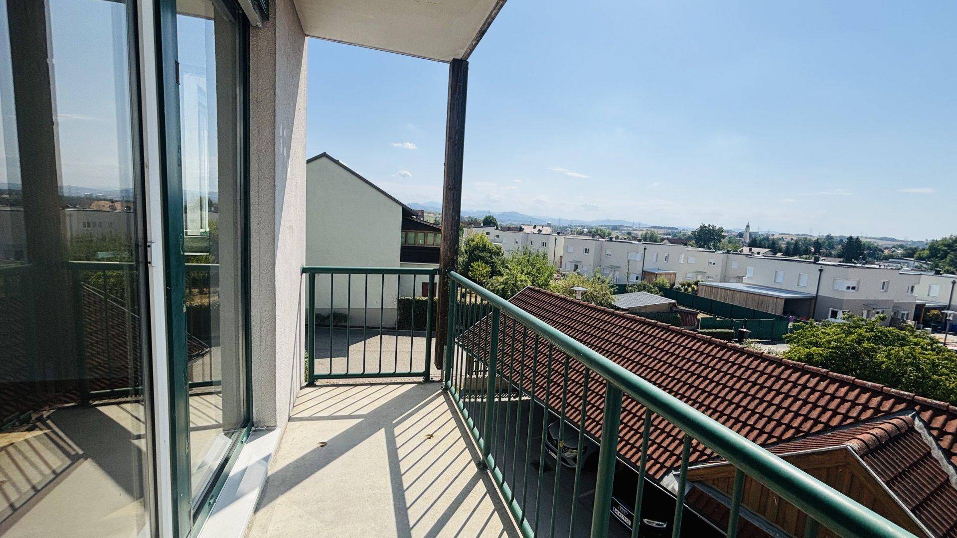 Heller Balkon mit grüner Brüstung und Panoramablick über die Stadt und die umliegende Natur.